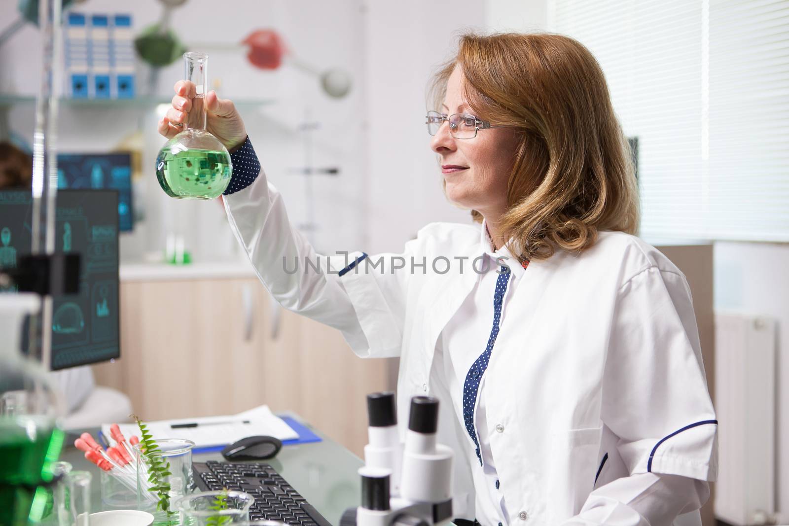 Middle age female biologist in a laboratory looking at chemical test tube. Product test.