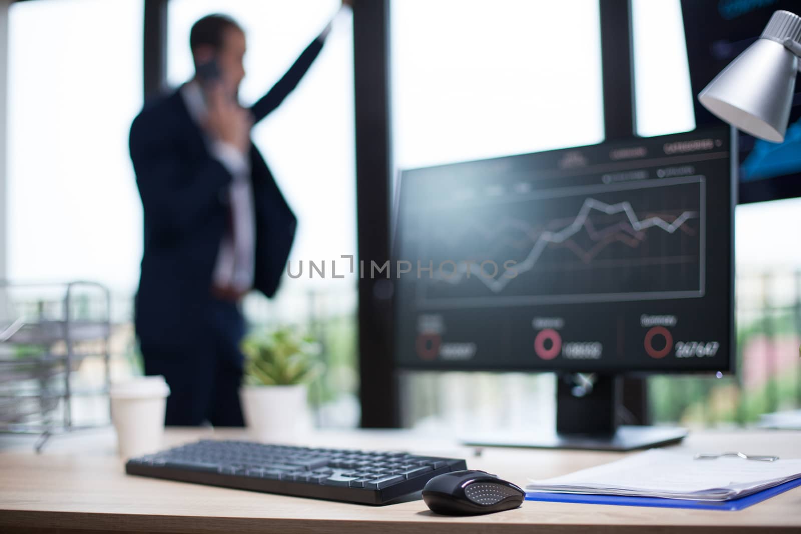 Corporate business office with graphics displayed on computer monitor. Bearded businessman in the background.