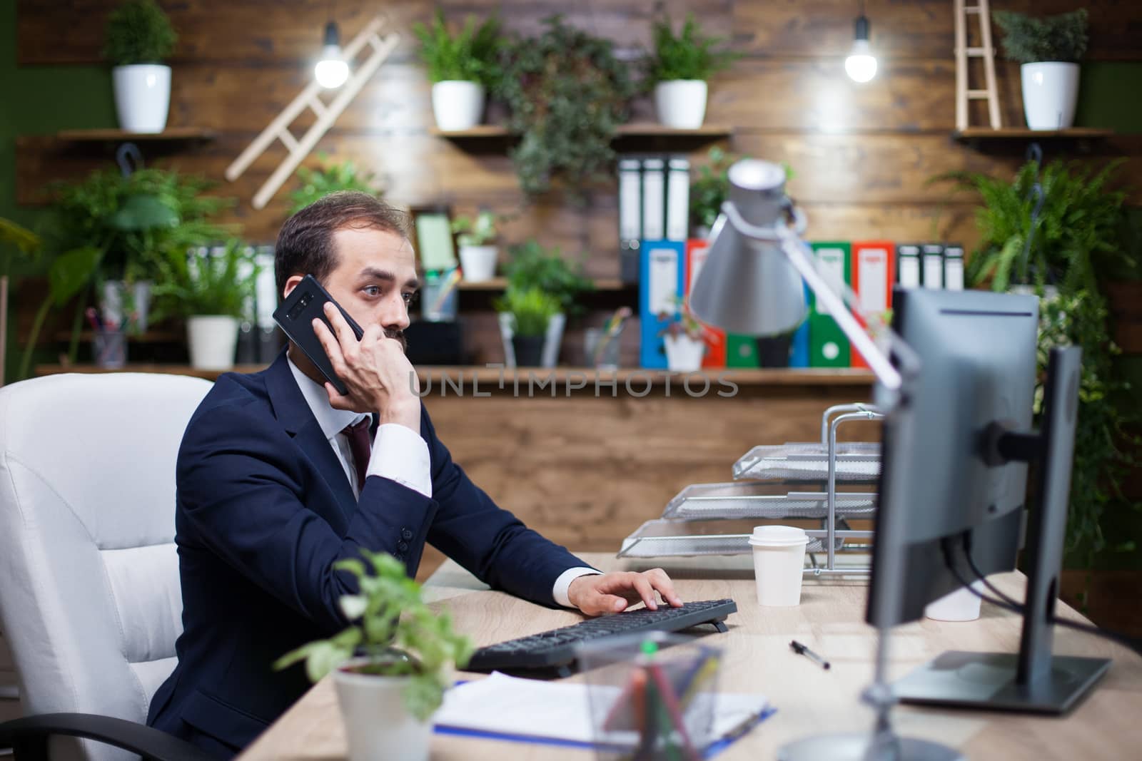 Young and successful business working on computer and having a business conversation on phone. Conversation about finances.