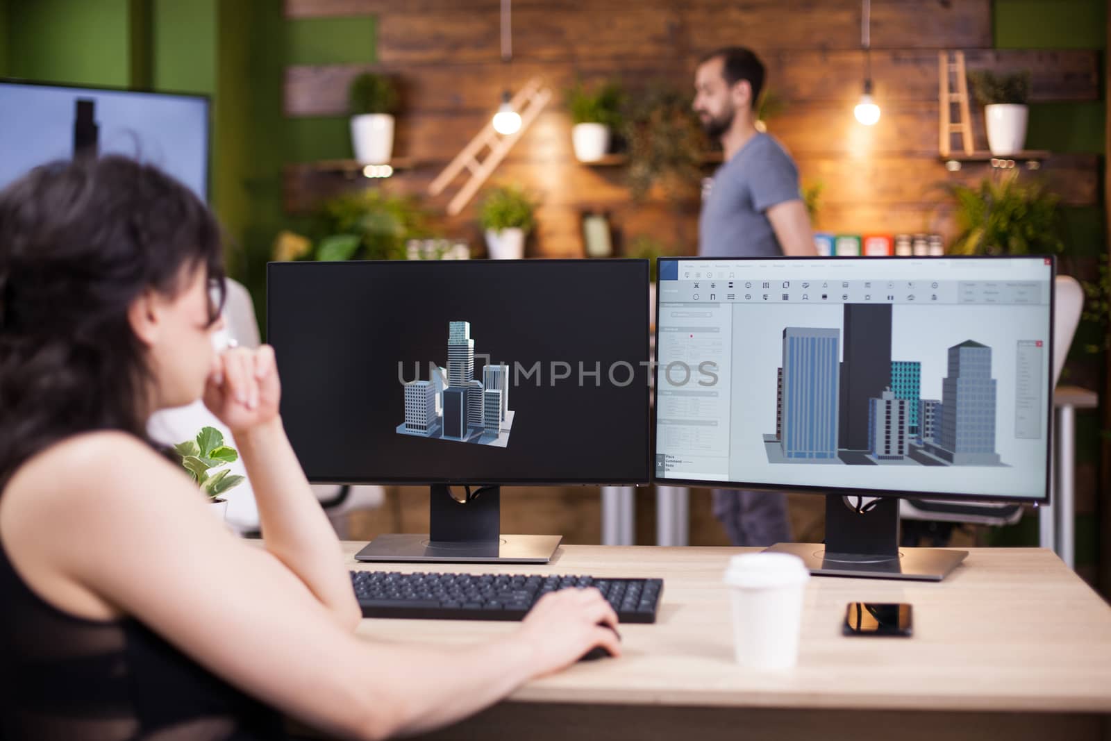 Young woman company director working on her computer. Employee working in the background. Pleased business woman.