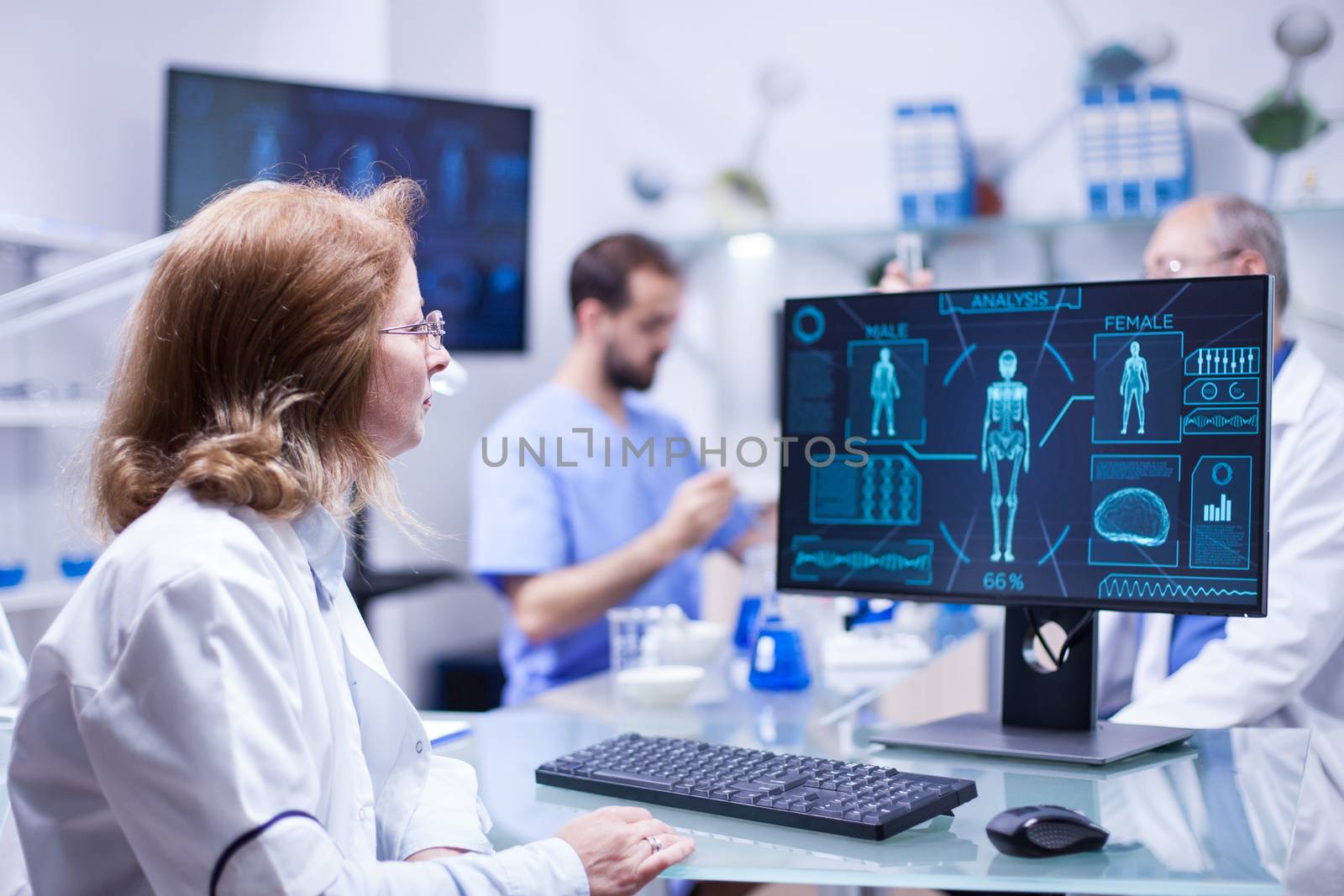 Female scientist looking at the monitor screen in research room. Chief of development working with test tubes in the background.