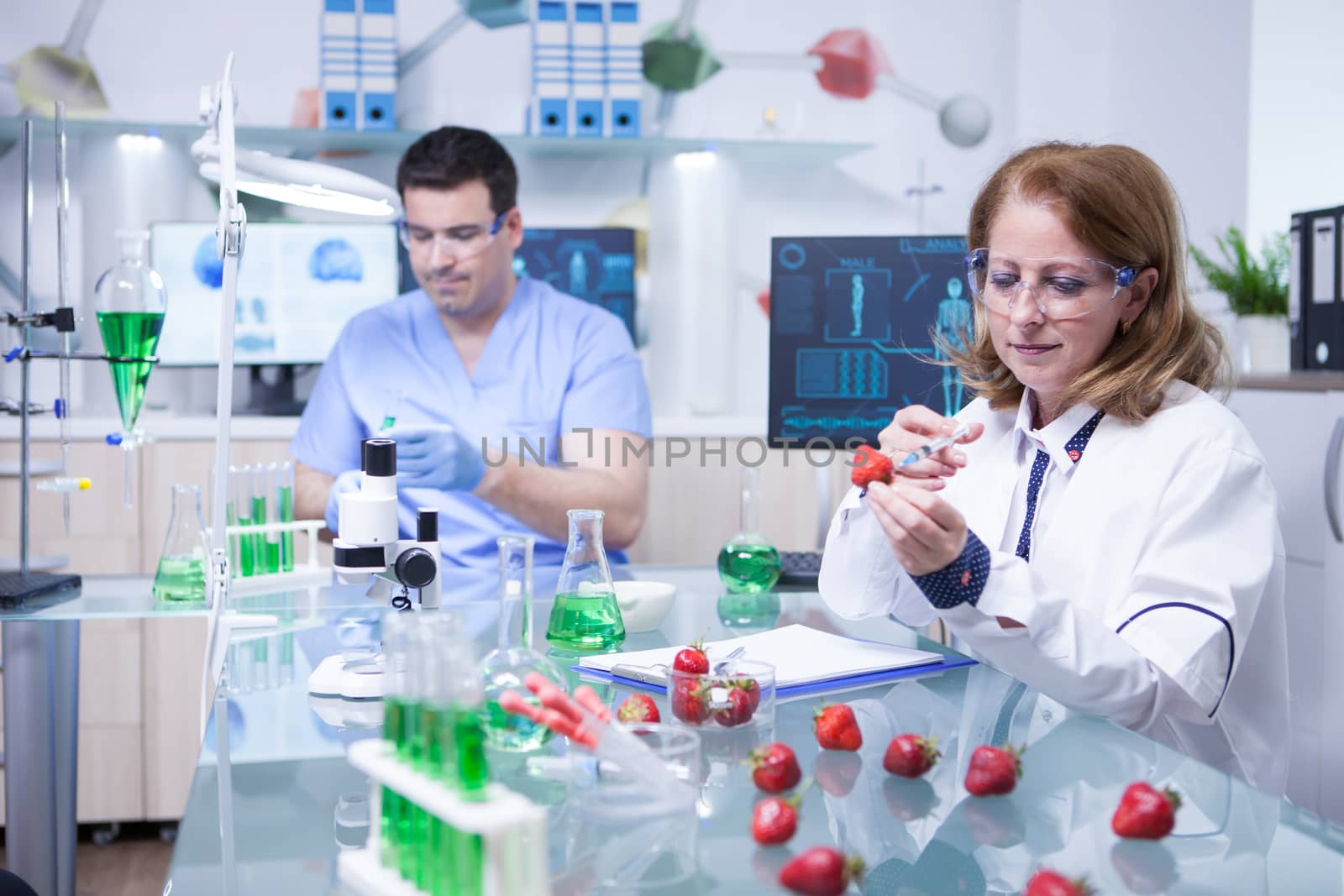 Biologist woman studying strawberries in a research lab. Scientist man working in the background.