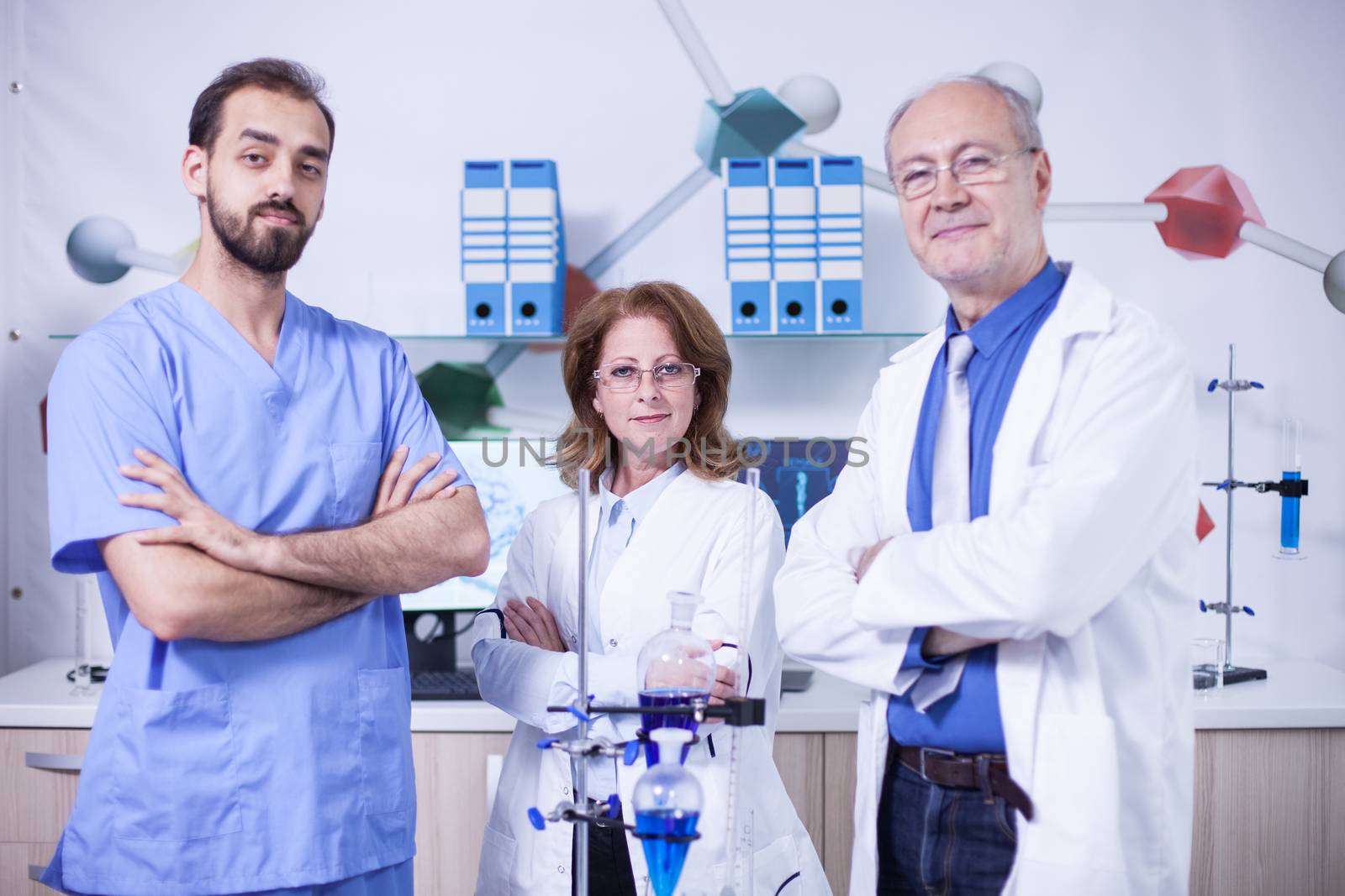 Portrait of three scientist dressed in their uniform in a laboratory. Senior scientist in white coat.