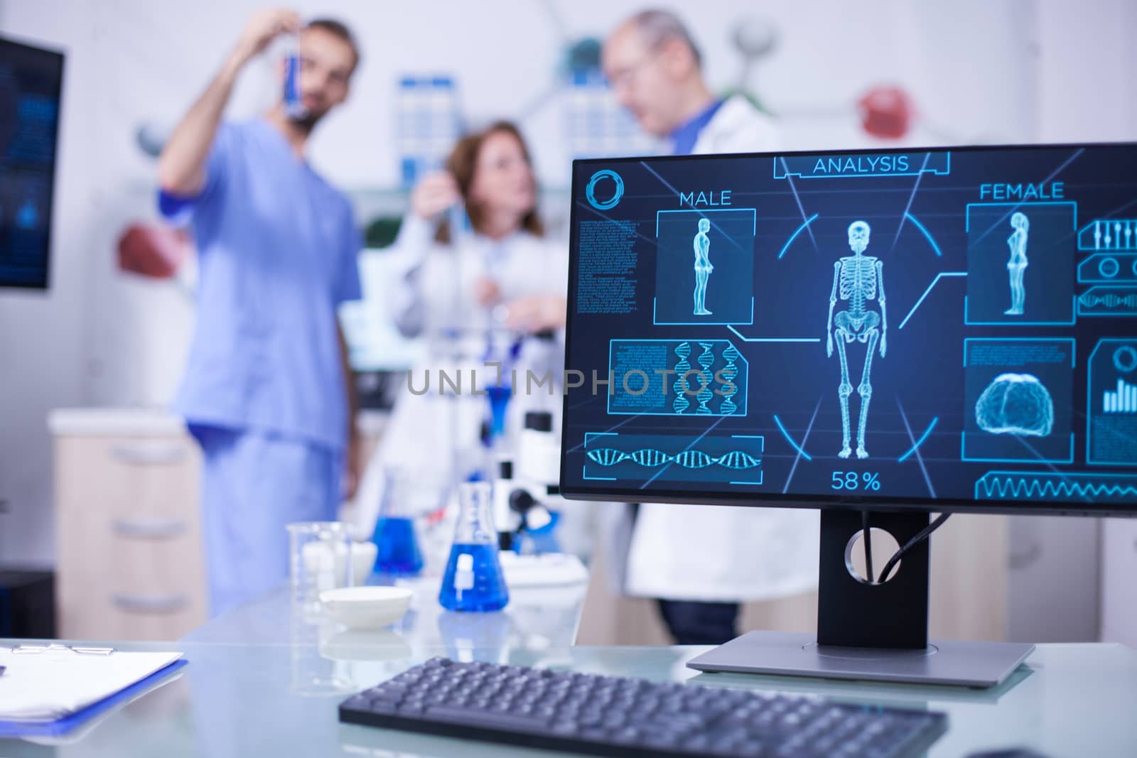 Display monitor in a hospital laboratory showing human skeleton. Team of scientist working in the background.