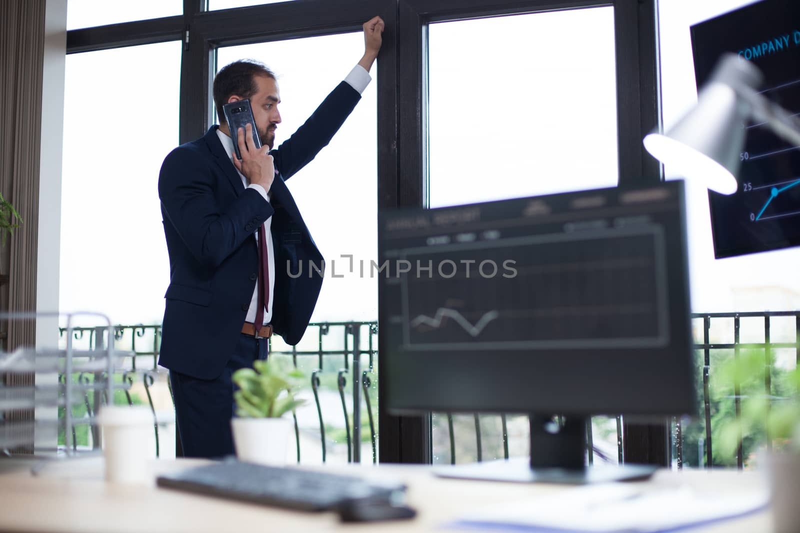 Focused young businessman having a phone conversation and looking on the window. Young entrepreneur in his office.