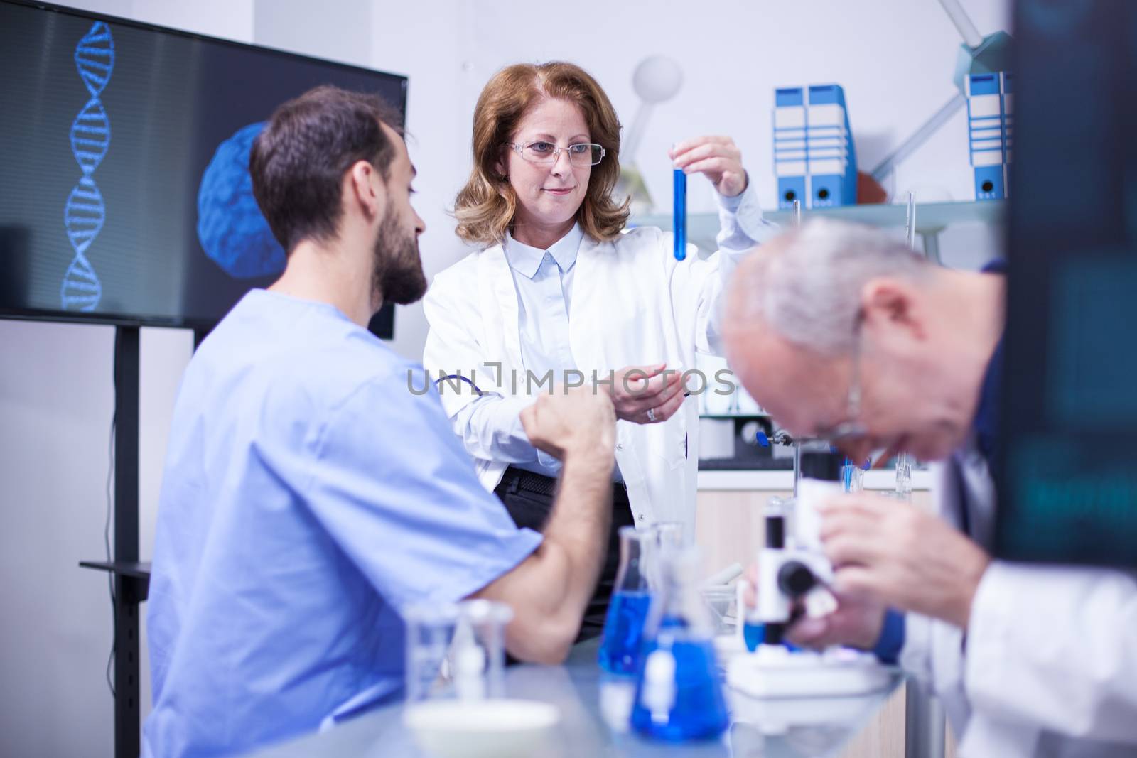 Middle age woman scientist working together with young technician in a laboratory. Senior engineer working on microscope in the background.