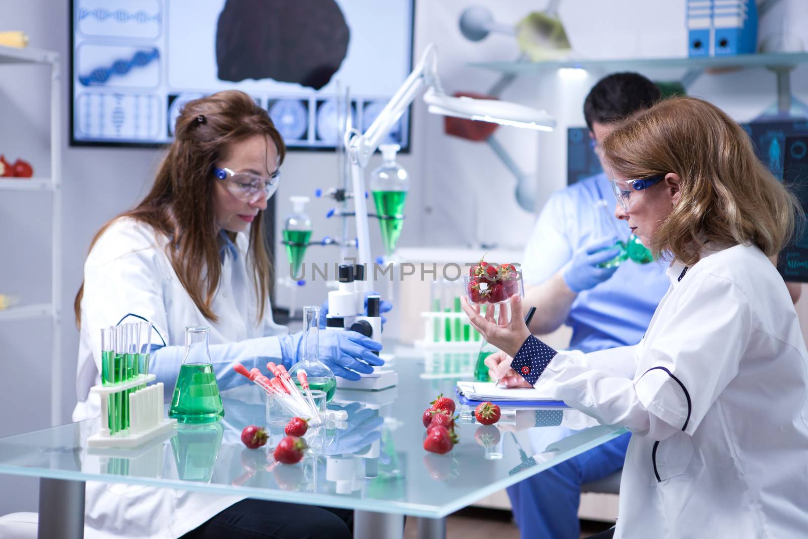 Caucasian female scientist holding a box of strawberries after doing biological tests. Microscope in a lab research.