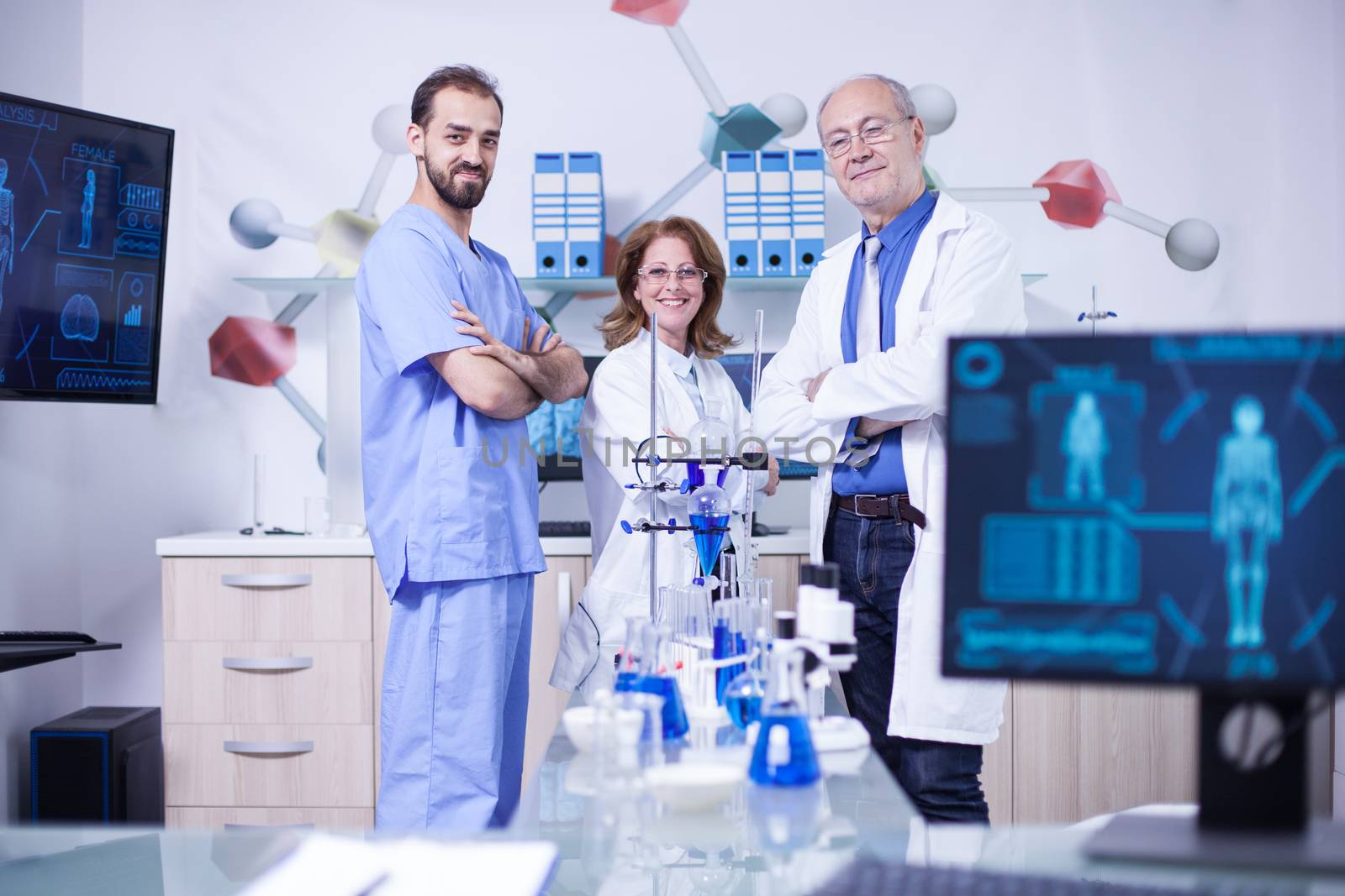 Smiling scientist colleagues in their uniform standing in chimical lab. Laboratory equipment.