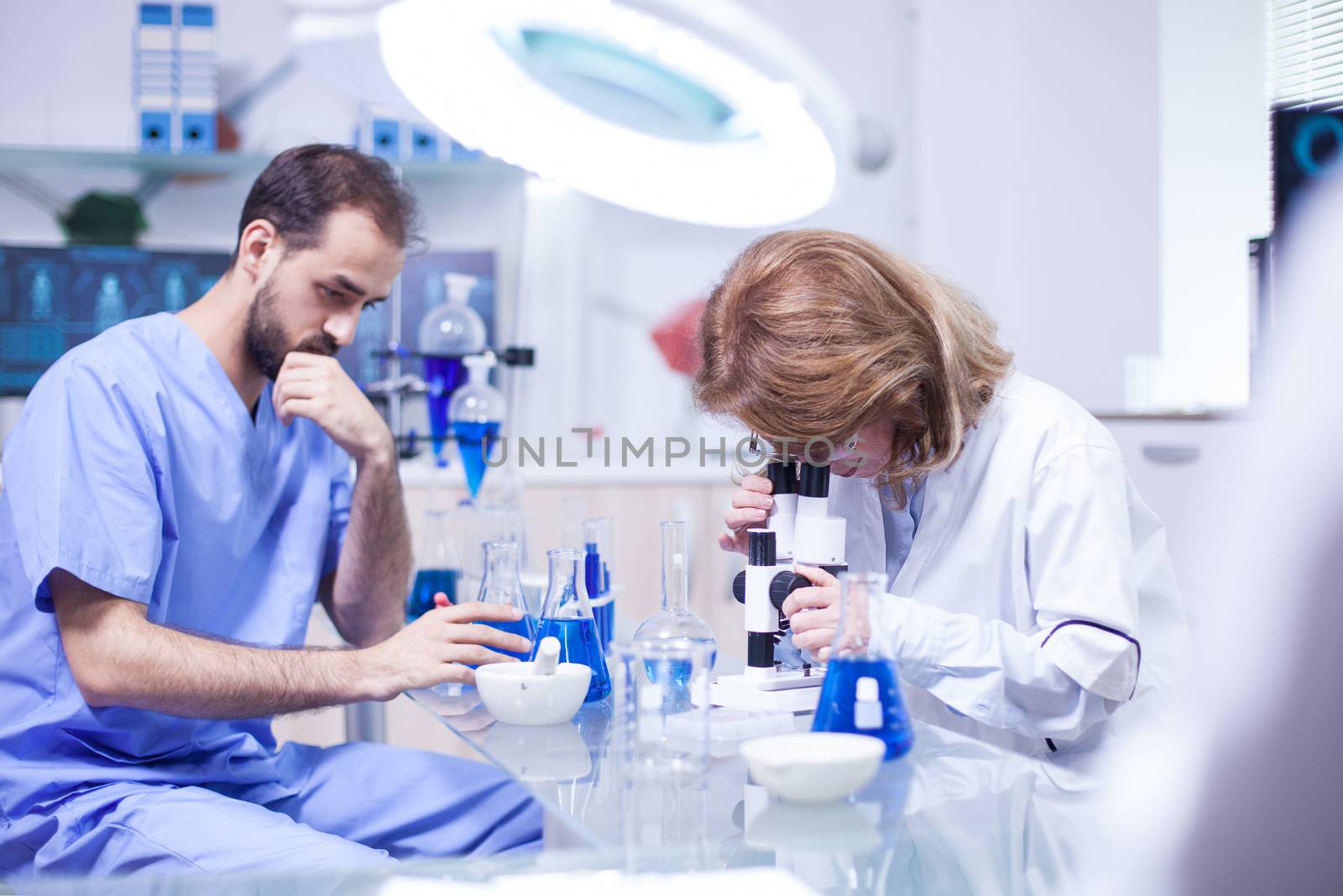 Middle age female scientist working with microscope in laboratory. Young caucasian male working as technician in a research laboratory.