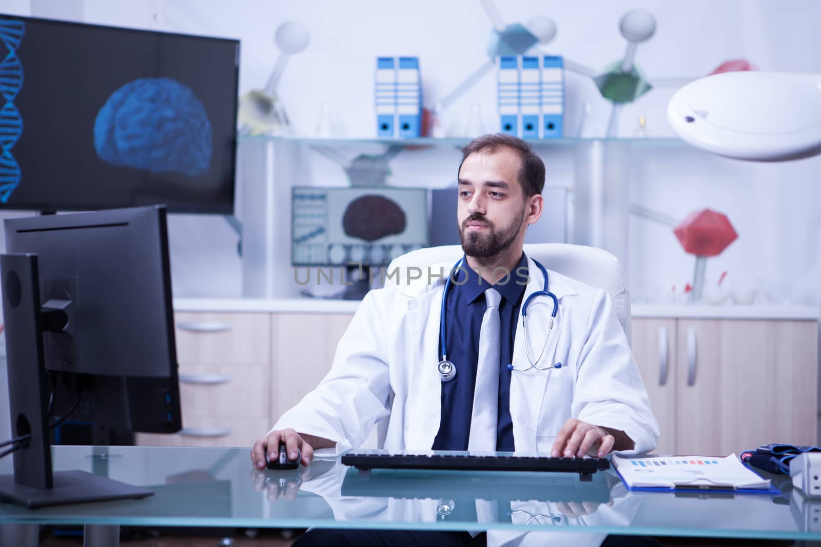 Attractive young doctor doing an online consultation using his computer at the clinic. Young bearded doctor working.