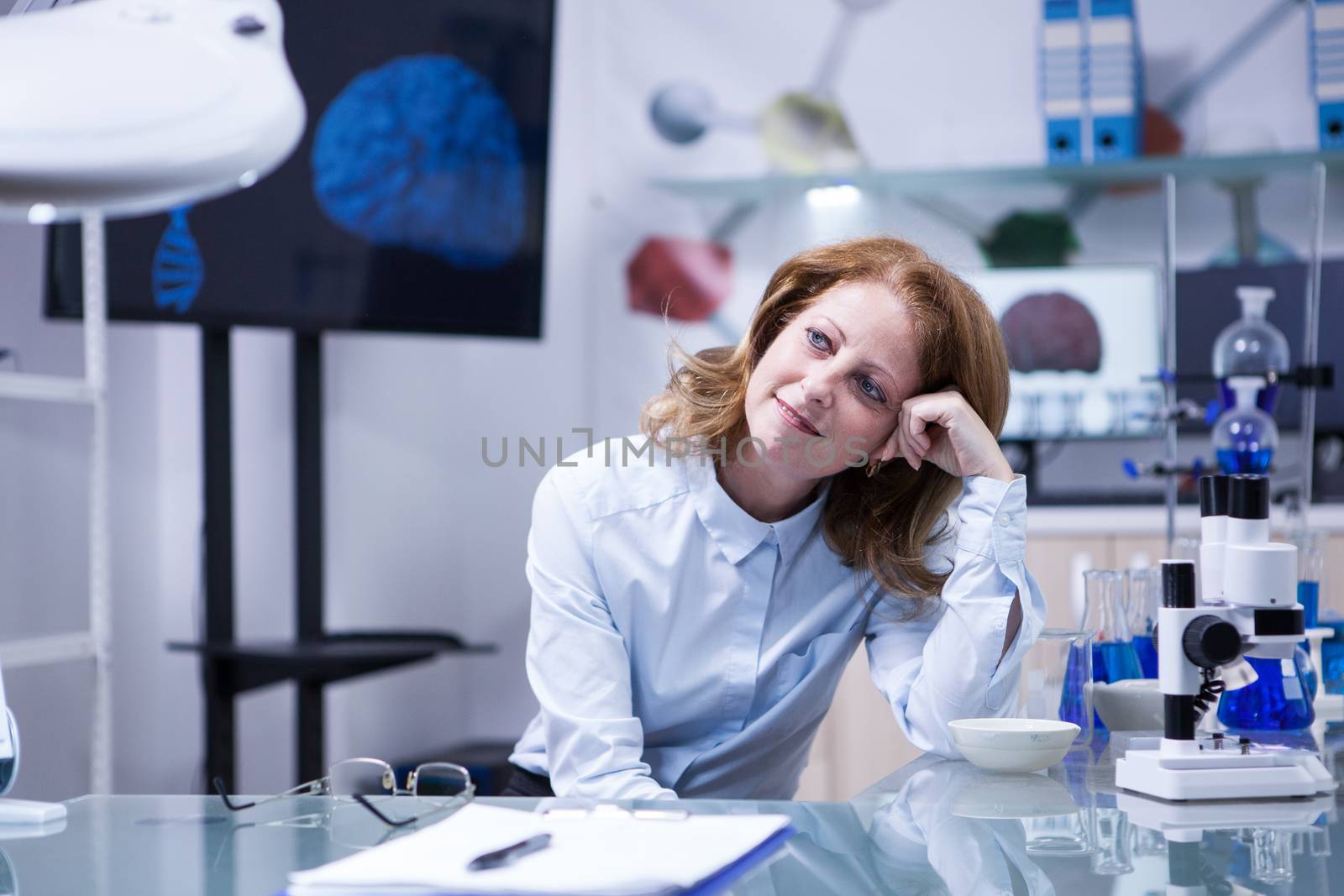 Middle age woman with red hair in a biomedical laboratory. Monitor with brain image in the background.