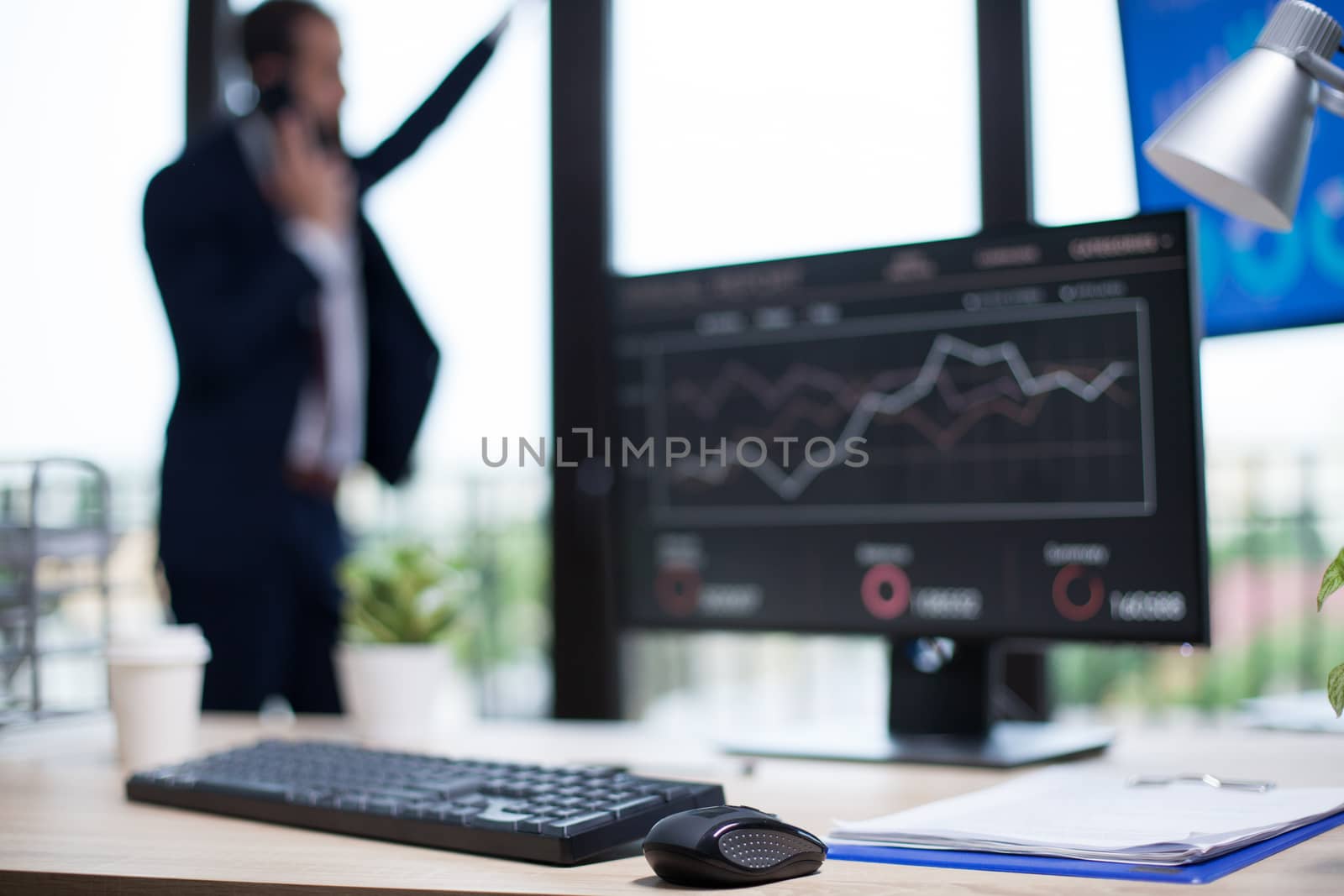 Business graphics displayed on computer monitor in entrepreneur office. Young bearded entreprenur in the background near the window.