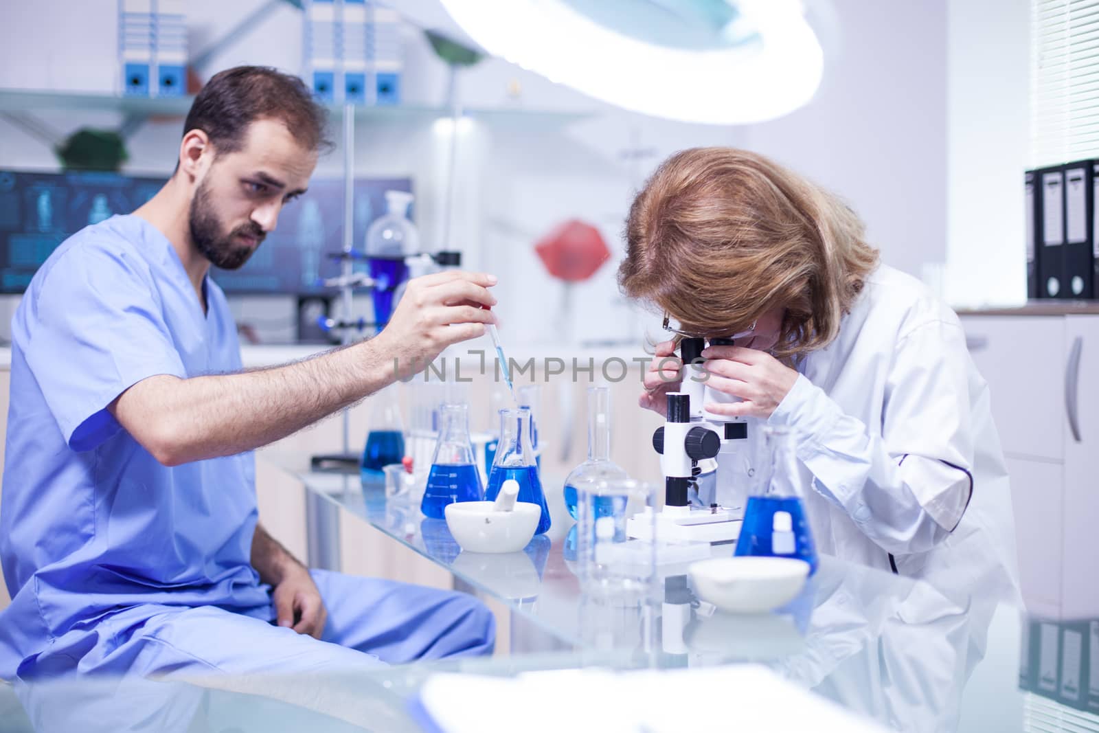 Young caucasian male scientist using a pipette analyzes a liquid to extract molecules in test tube. Female scientist adjusting microscope.