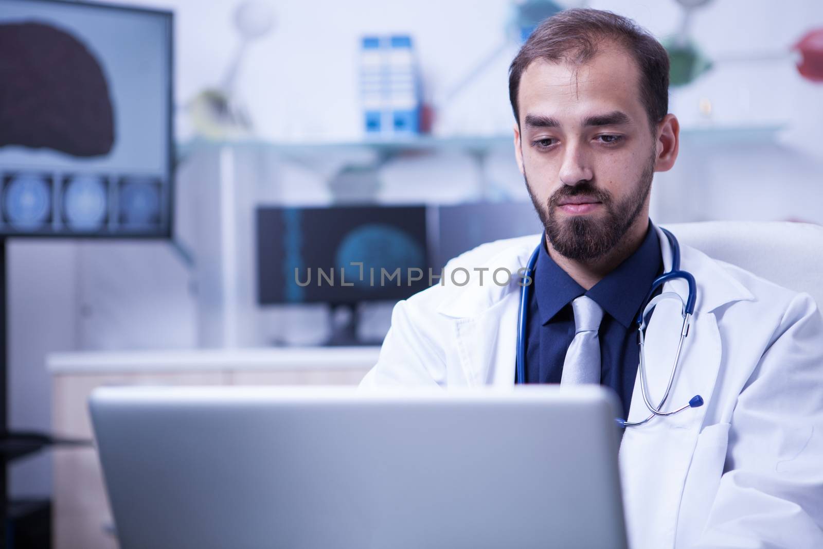 Close up portrait of handsome doctor sitting at his desk and working on computer. Specialist doctor on brain treatment.