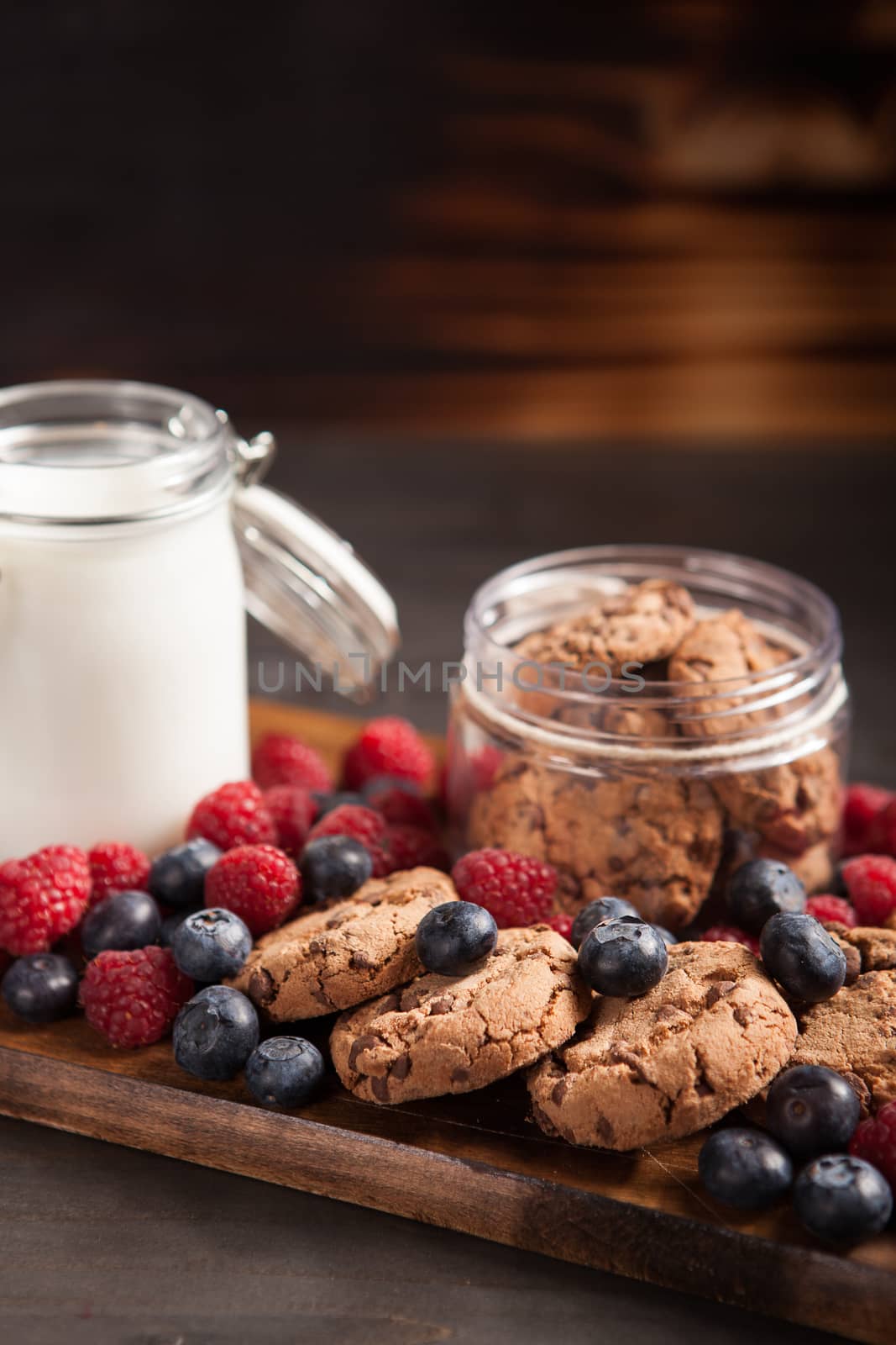 Delicious oatmeal cookies with fresh raspberries and milk over rustic wooden table. Tasty bakery.