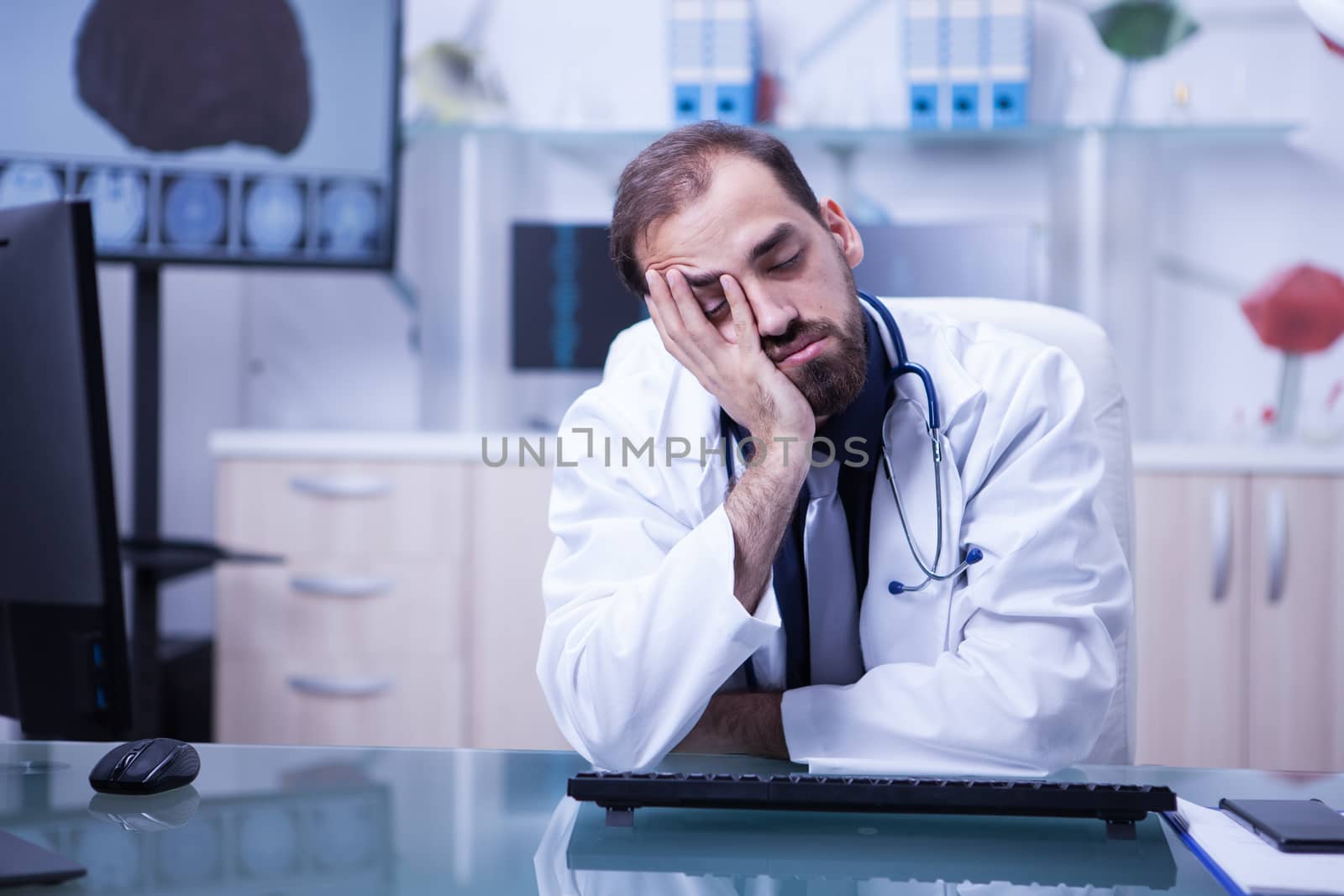 Portrait of tired male doctor sleeping on his desk after a long day at the hospital. Overworked and stressed doctor.