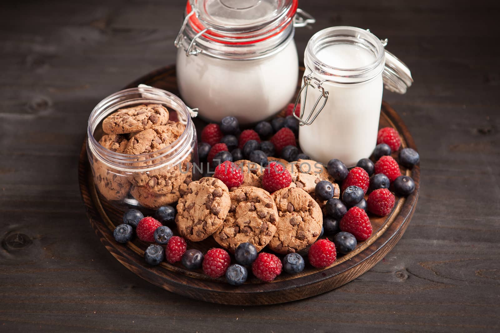 Wooden plate full of delicios and tasty biscuits next to fresh bluebarries. Fresk milk for cookies.