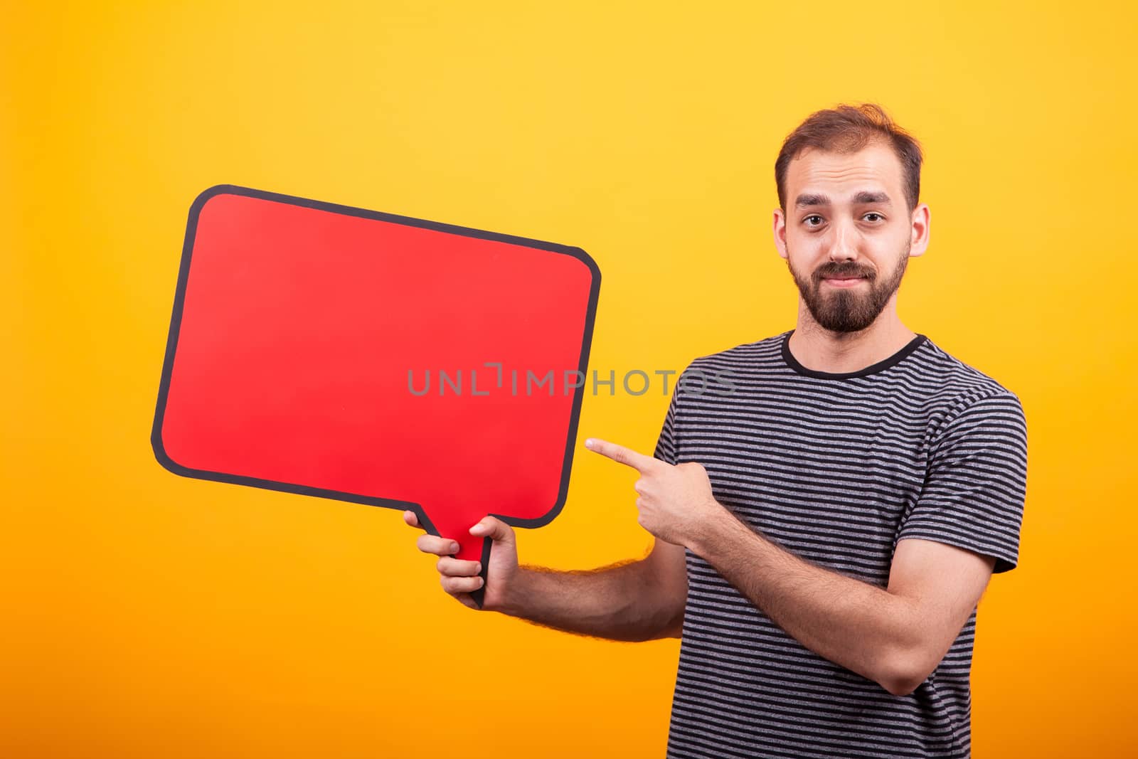 Portrait of young bearded man pointing at his informing board over yellow background. Cheerful young man.