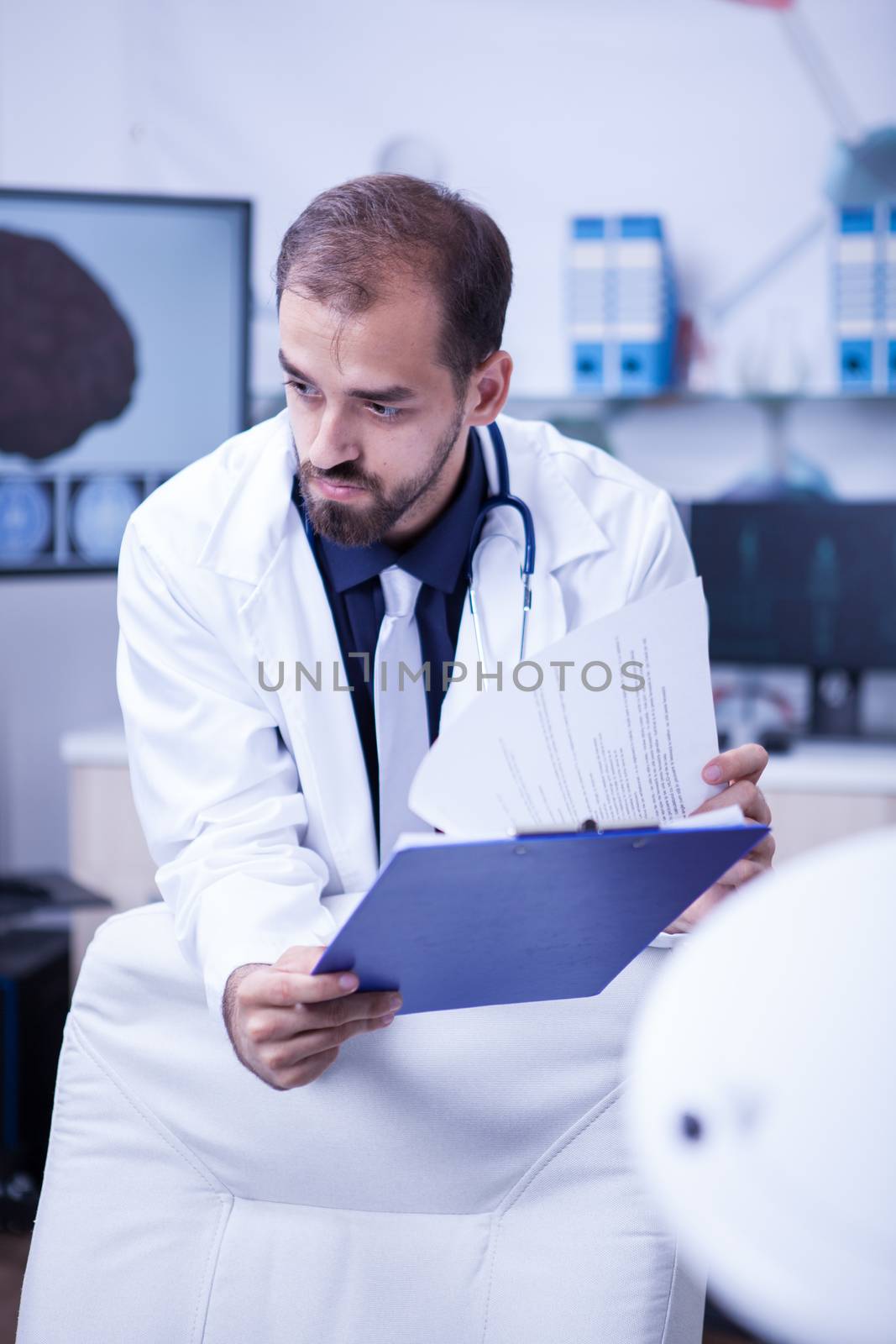 Close up portrait of brain surgeon looking into his notes from clipoard. Doctor in uniform at hospital cabinet.