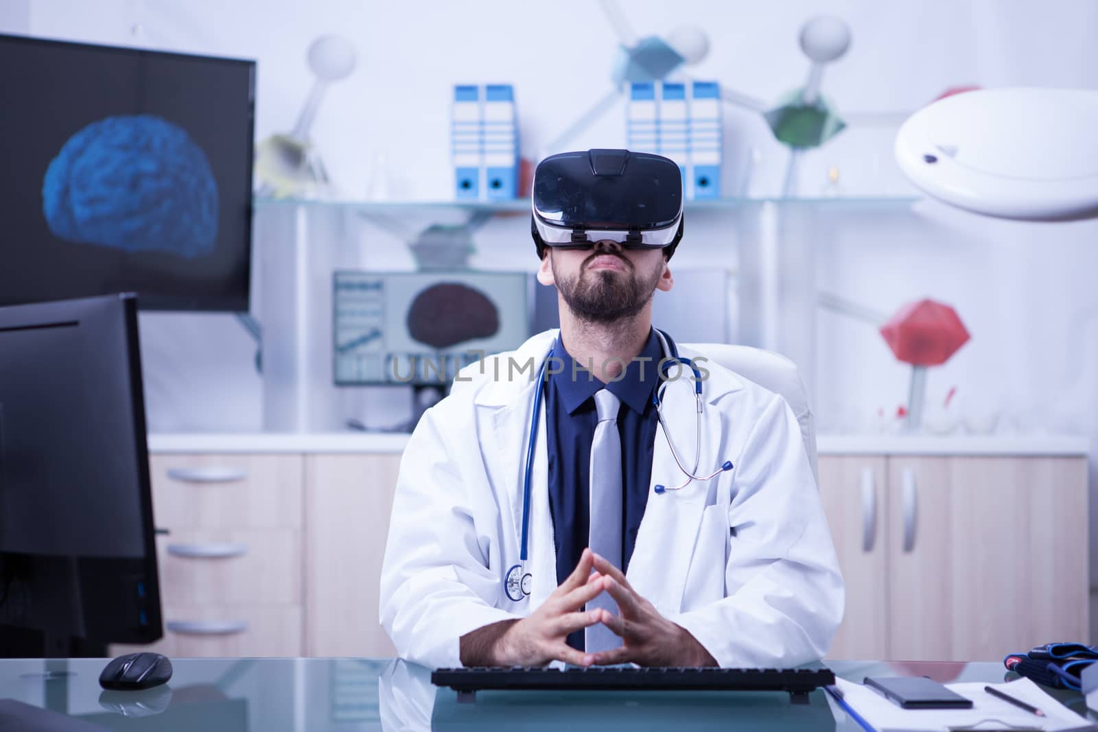 Portrait of doctor sitting at his desk using virtual reality headest looking up. Doctor using modern techology.