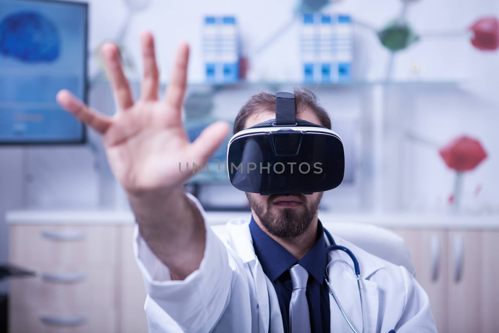 Close up portrait of young doctor wearing virtual reality goggles reaching out with his hand. Adult doctor with modern technology.