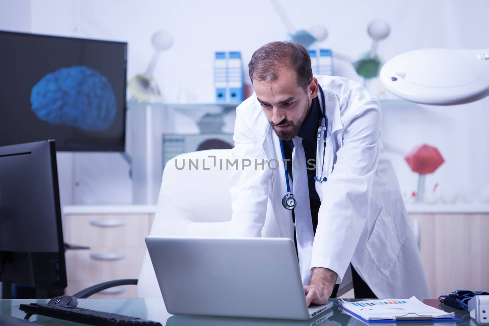 Doctor working on his laptop and checking the treatment of his patients. Attractive doctor with a white coat.