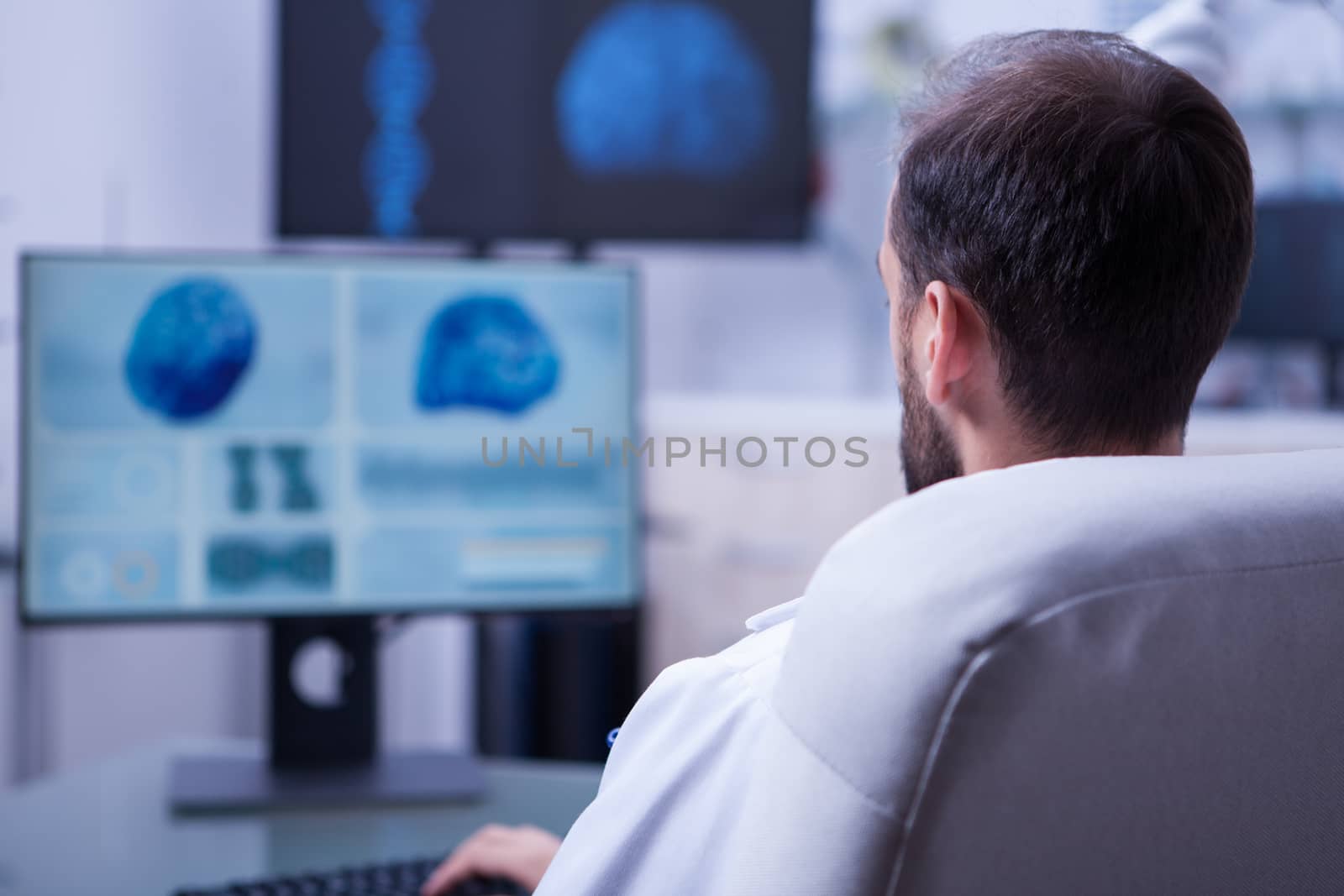 Young bearded doctor typing a diagnostic for a patient on his computer keyboard. Doctor in hospital office.