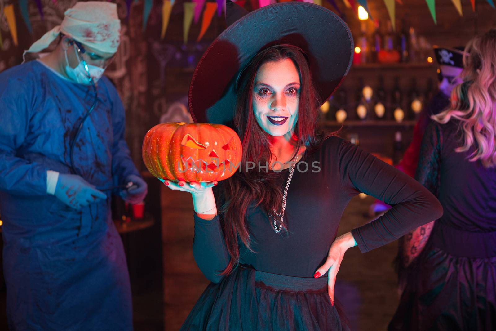 Friends celebrating halloween looking like scary monsters. Girl holding a pumpkin and looking at the camera.