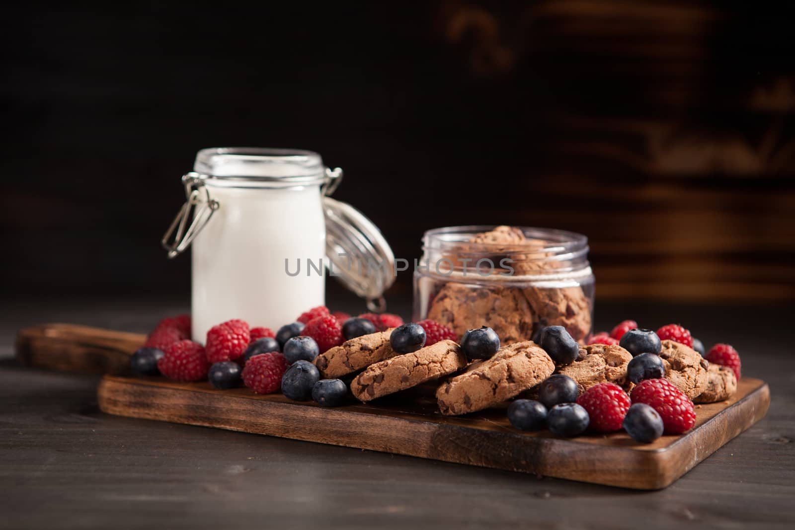 Delicious brown cookies on wooden plate with fresh bluebarries. Organic milk.