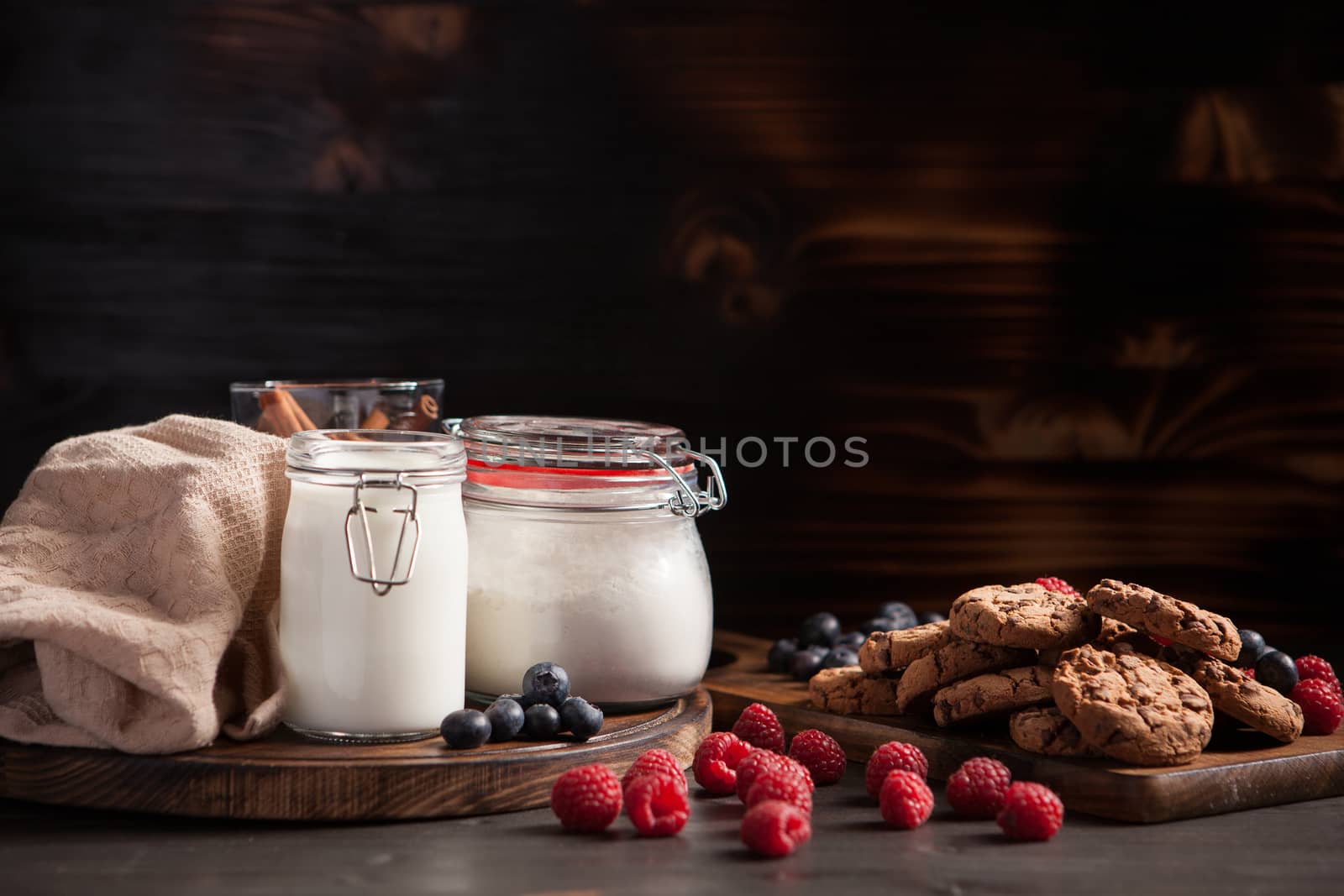 Delicious cookies with dark chocolate and blueberries over rustic wooden table. Stacked cookies with milk.