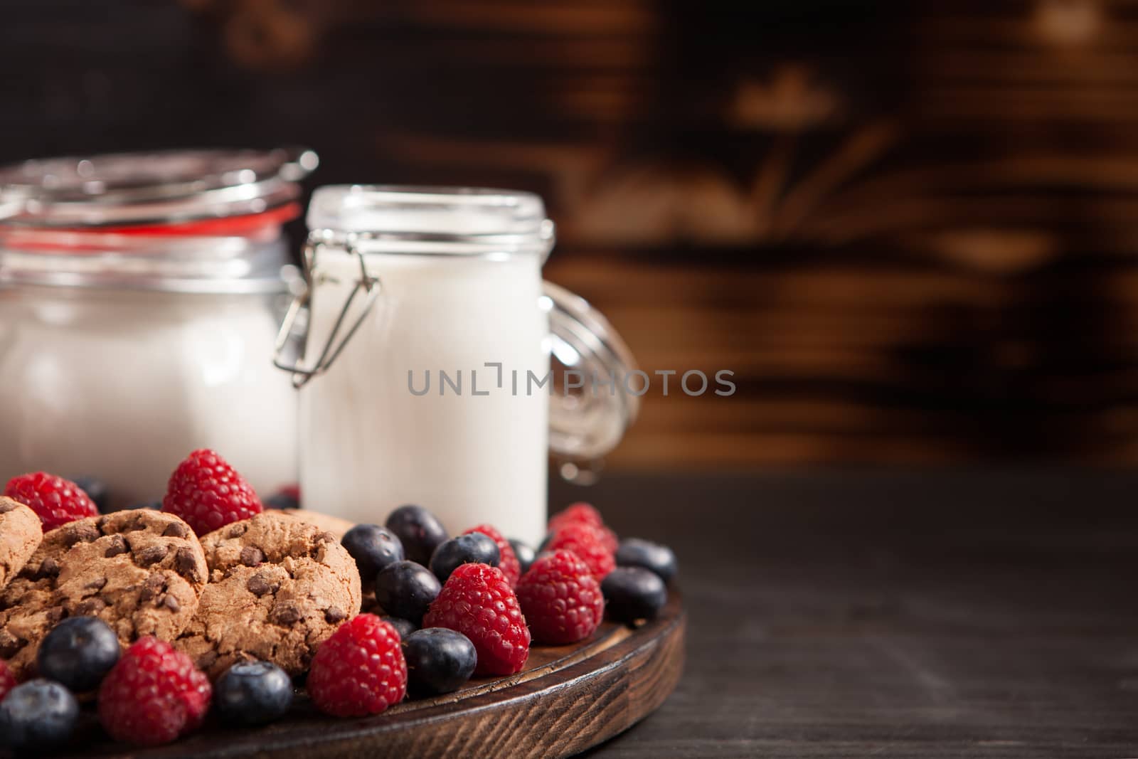 Freshly baked oatmeal chocolate biscuits out of the over with fresh milk on wooden plate. Copy space available.