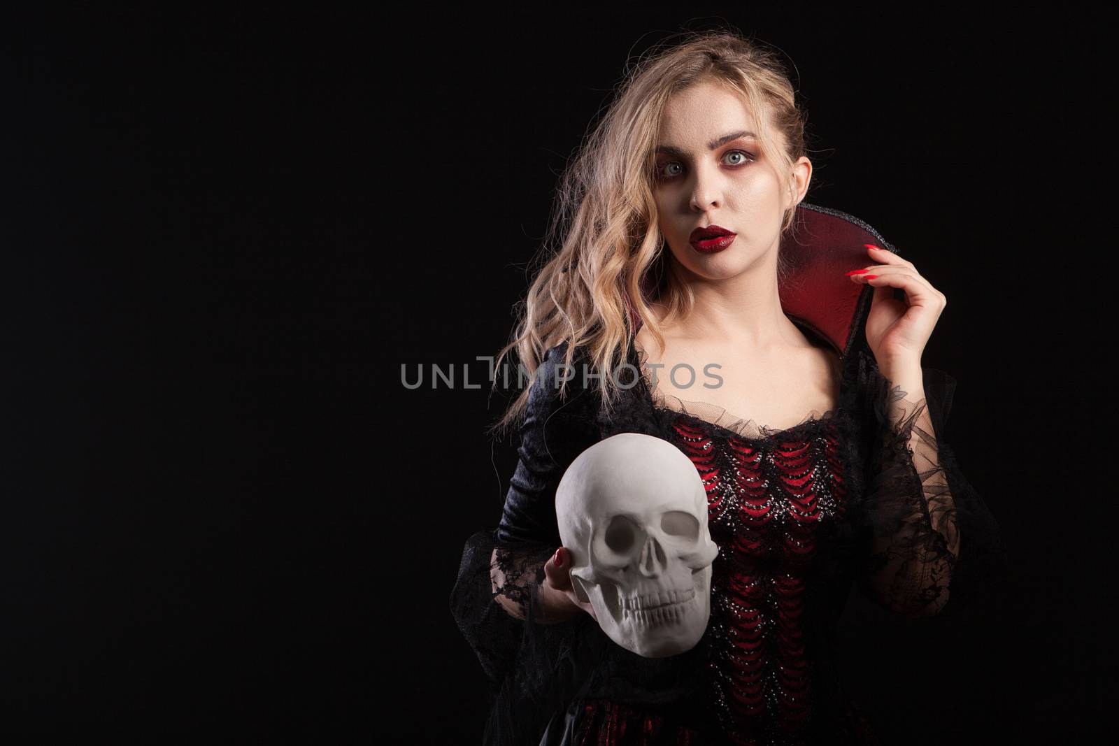 Amazing dead girl dressed up like vampire holding a skull for halloween carnival. Portrait of woman in vampire costume.