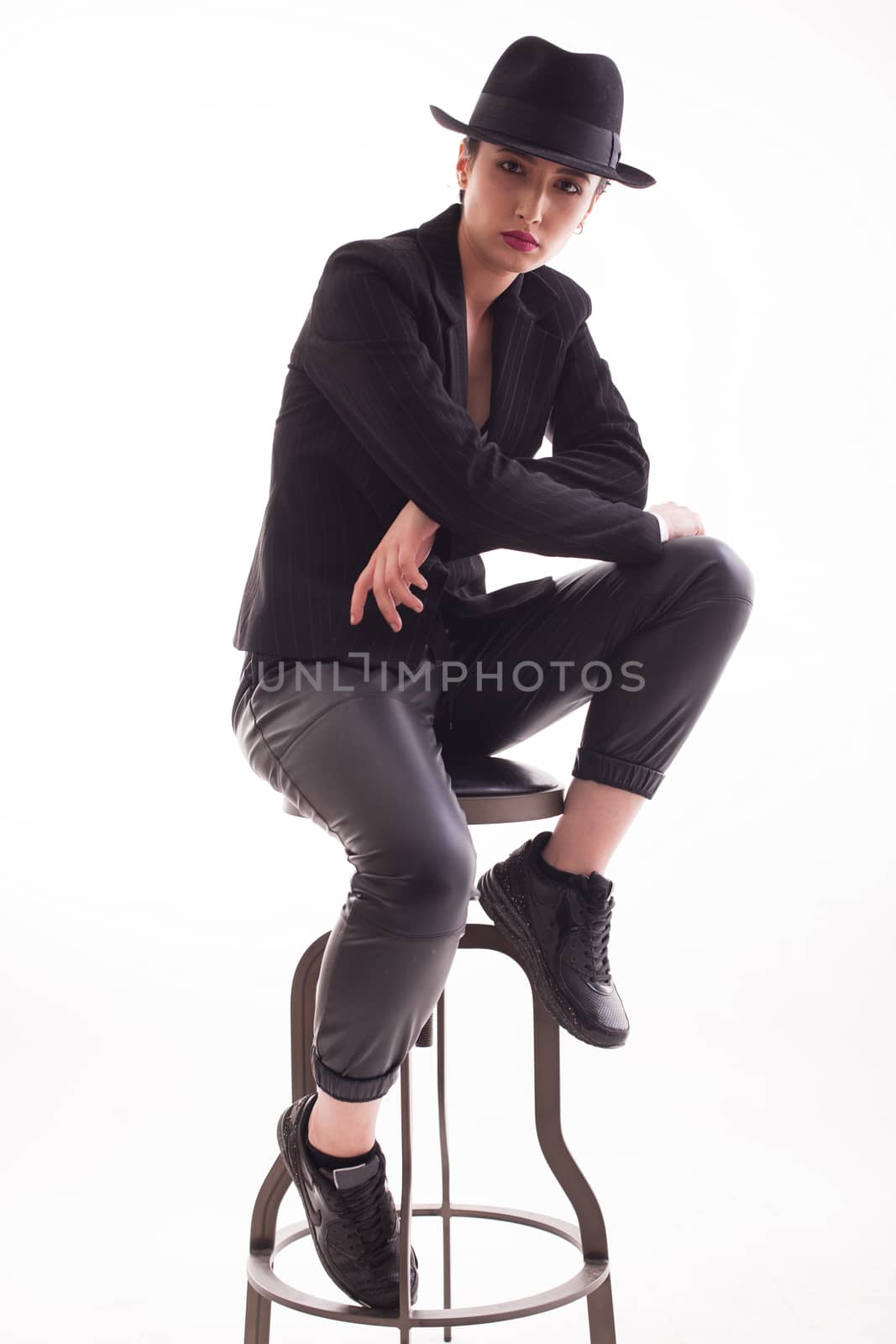 Caucasian beauty with a stylish hat sitting on a chair over white background in studio Elegant and stylish woman.