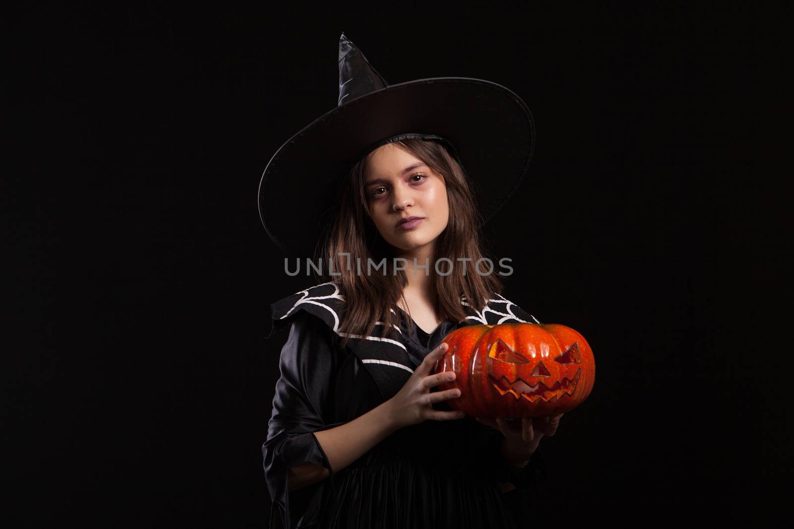 Little girl with a serious expression making a spell while holding a pumpking for halloween. Child dressed up for halloween carnaval.