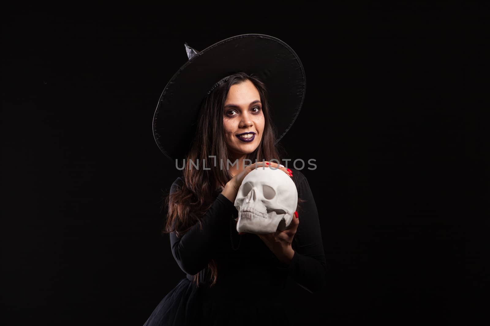 Pretty young woman in a witch costume for halloween party doing evil witchcraft. Portrait of woman doing magic on a human skull.