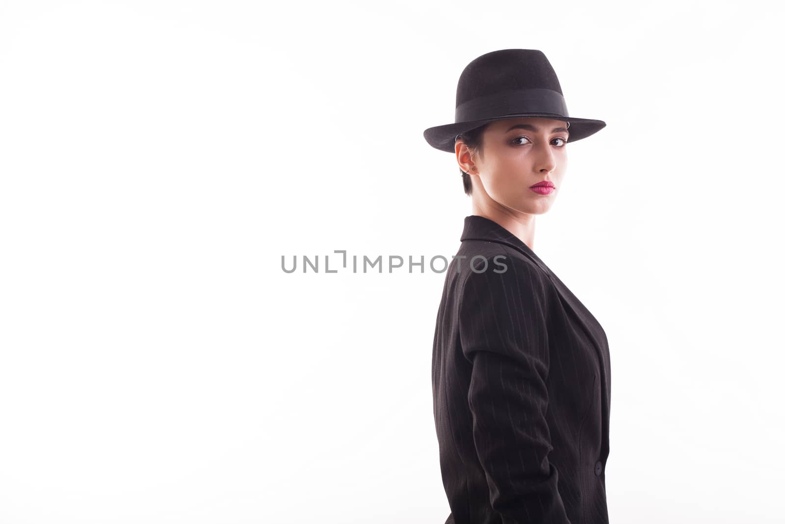 Fashionable caucasian young model posing with a black hat in studio over white background looking at the camera. Copy space available.