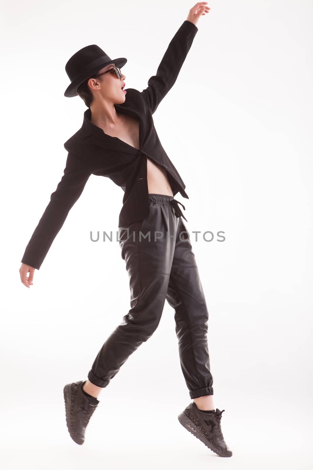 Beautiful fashion model jumping in the air posing wearing stylish clothing over white background in studio. Retro hat.