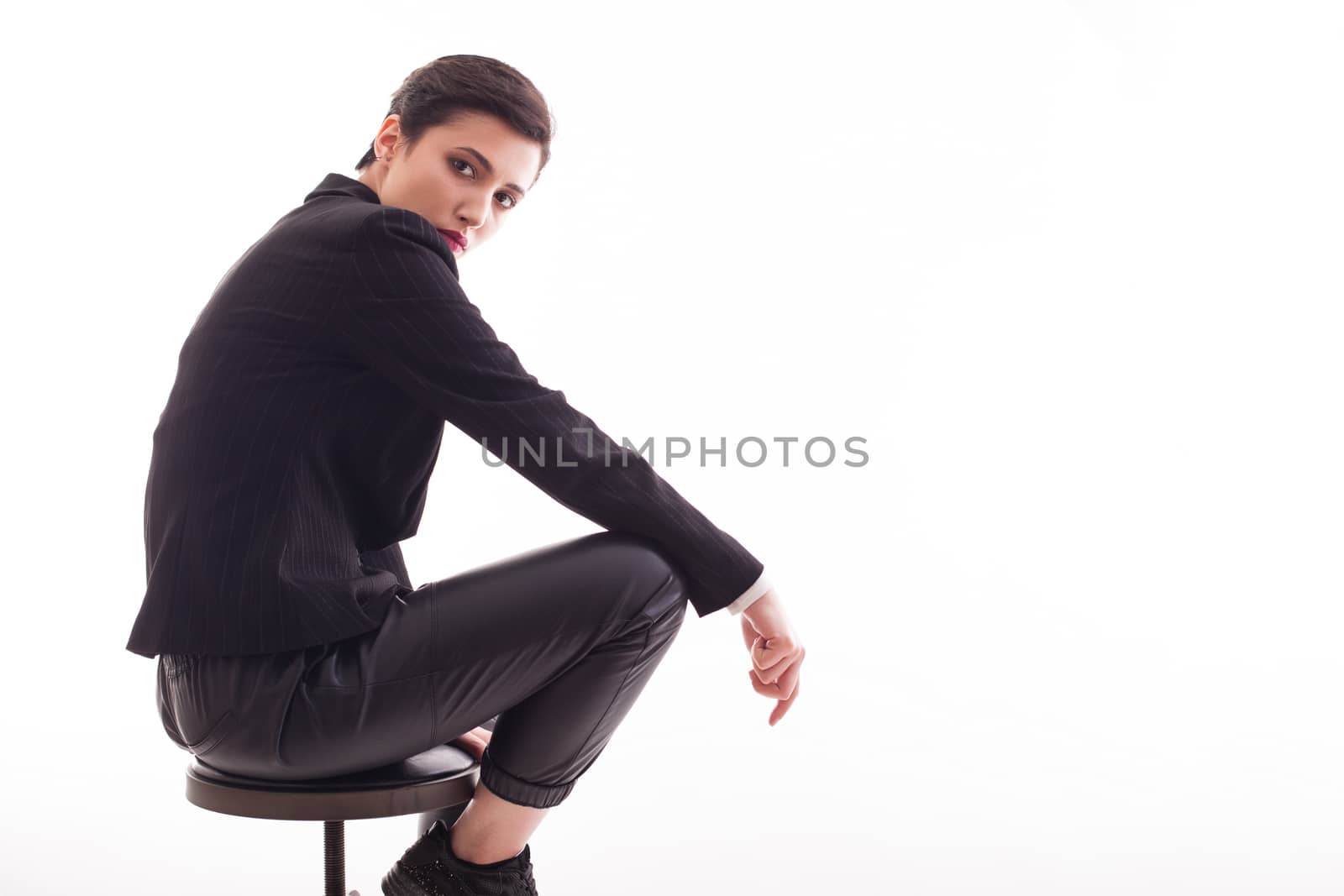 Portrait of stylish young woman posing in studio sitting on a chair over white background. Copy space available.