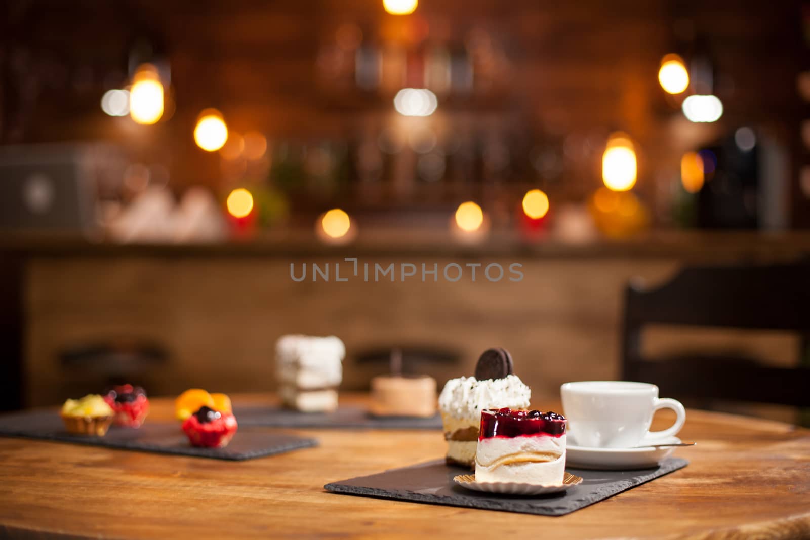 Composition of different cakes with tasty flavours over a wooden table in a coffee shop. Tasty mini cakes with fruits. Cakes with delicious biscuit on top.