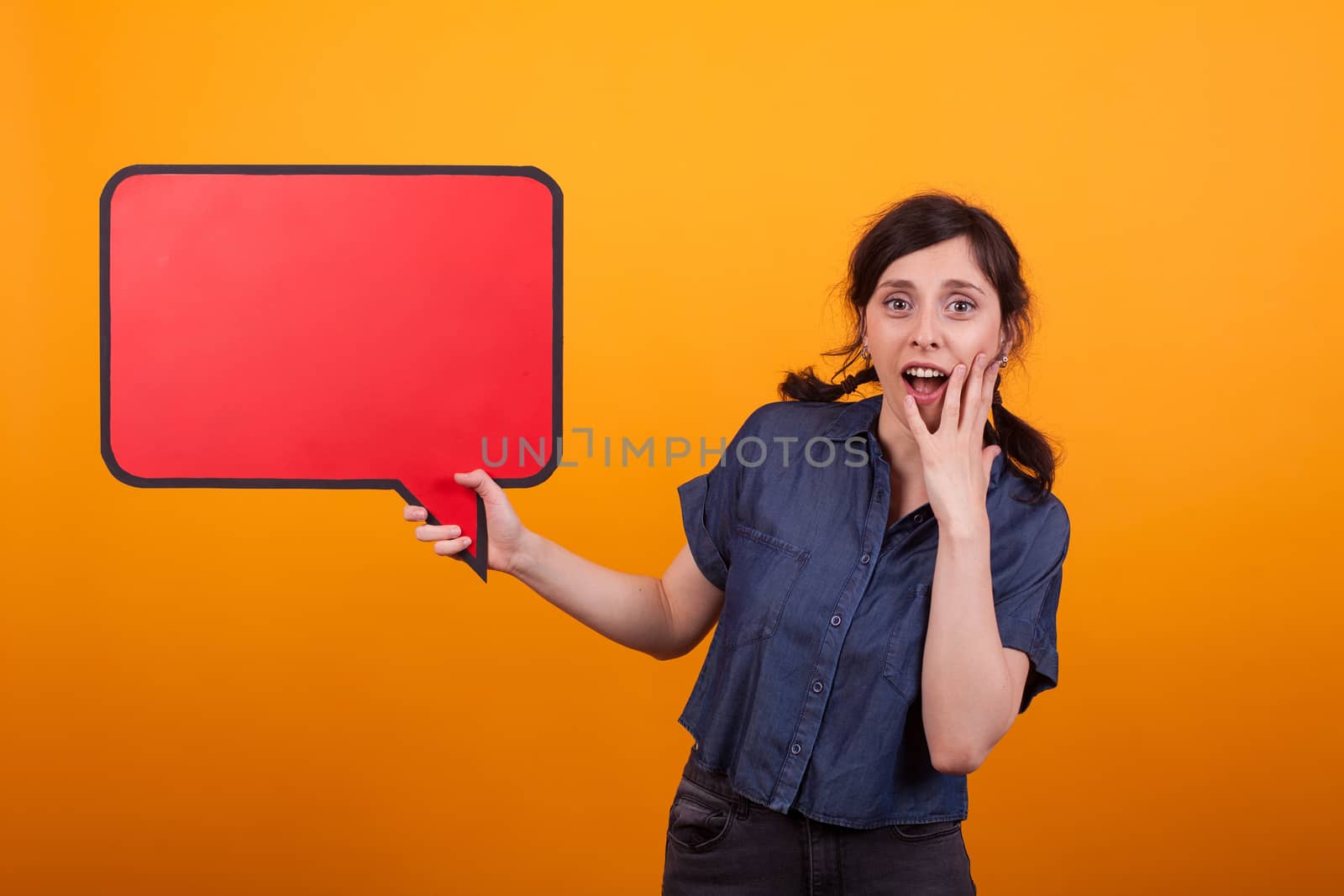 Shocked young woman with a speech bubble against a yellow background in studio. Surprised woman with thought bubble.