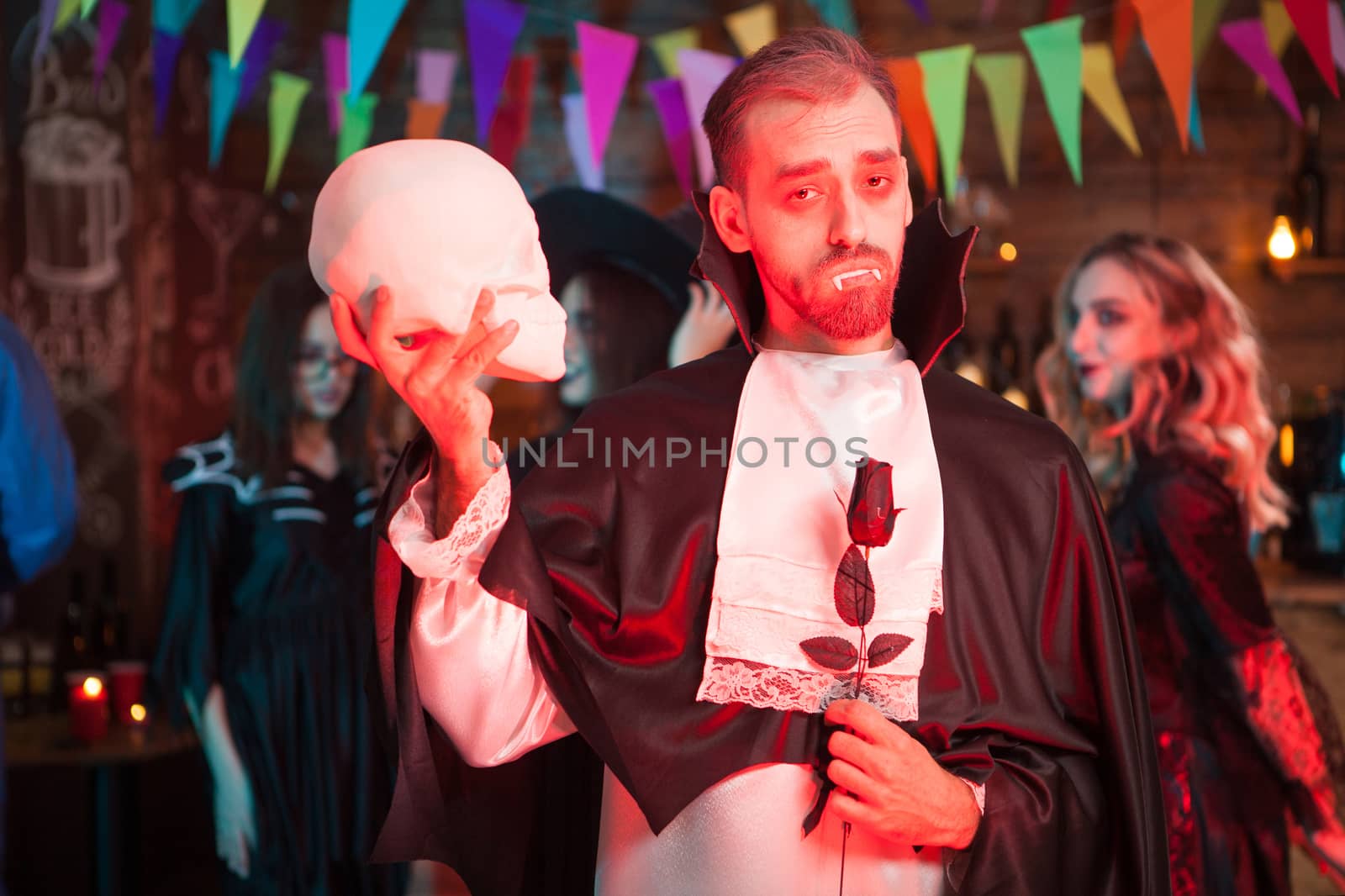 Scary man in dracula costume with a skull in his hand looking at the camera at halloween party. Scary man at halloween party.
