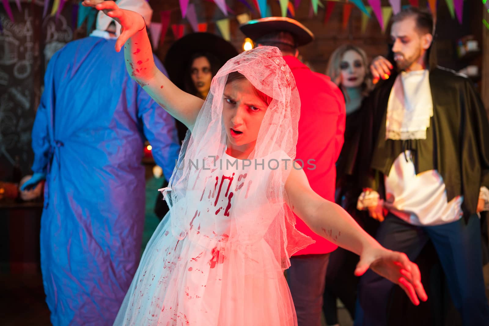 Little bride with creepy face looking at the camera at halloween party. Dracula in the background.