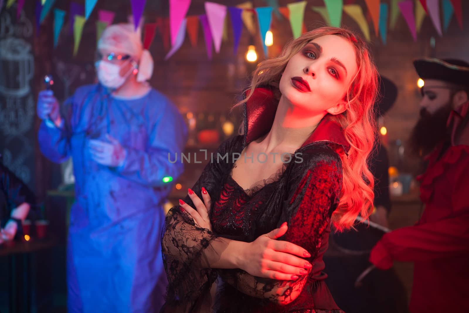 Side view portrait of beautiful young woman dressed up like a witch with a serious face at halloween gathering. Man dressed up like a doctor in the background at halloween celebration.
