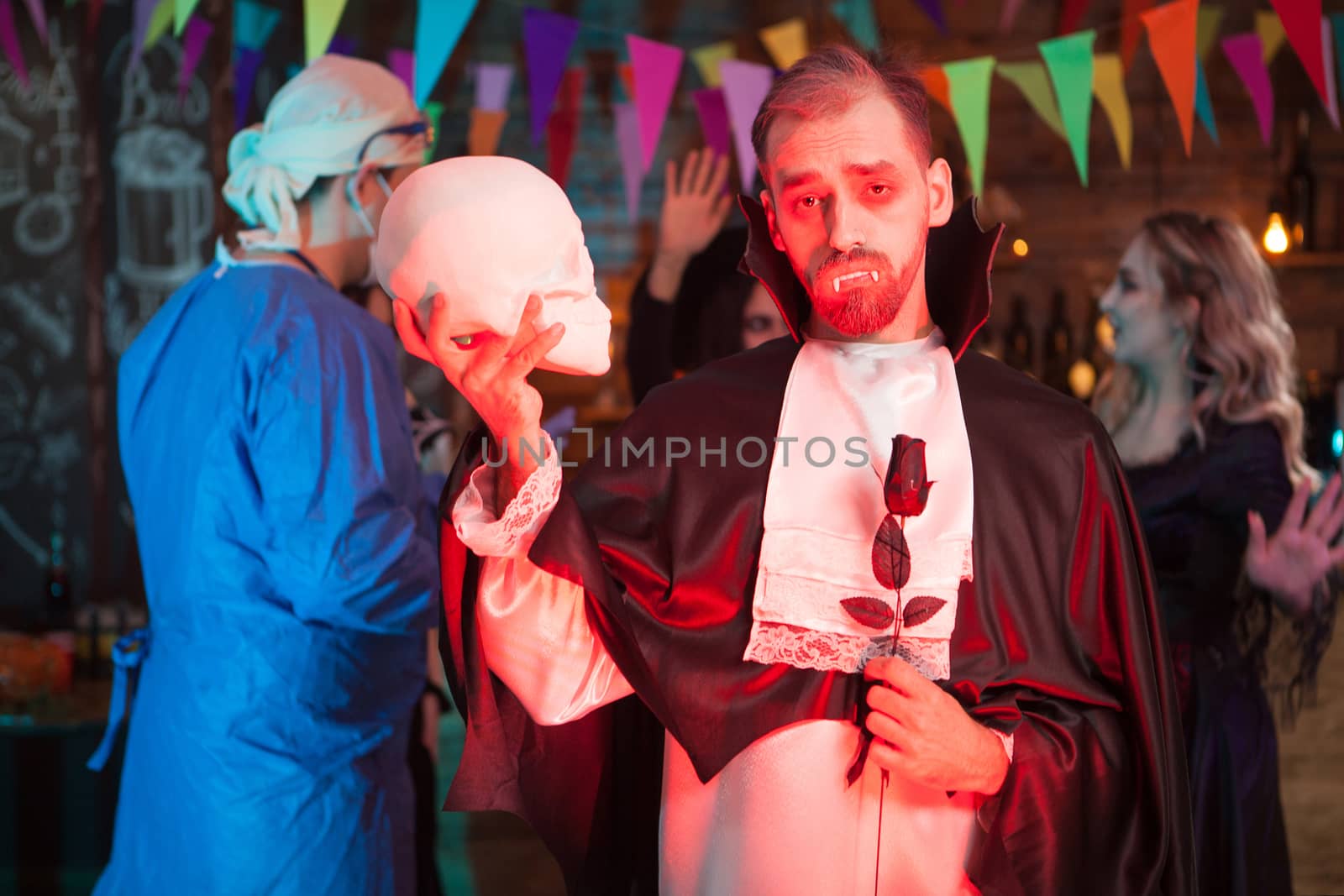 Count dracula holding a human skull and looking into the camera at halloween celebration by DCStudio