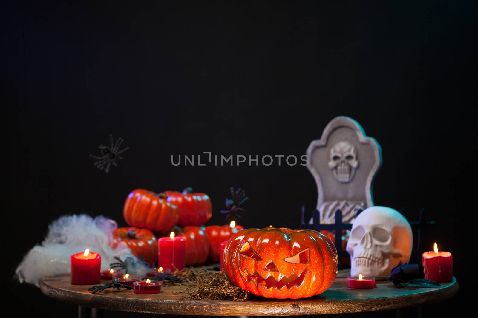 Carved scary pumpking sitting on a wooden table with a creepy skull at halloween celebration. Halloween decoration.