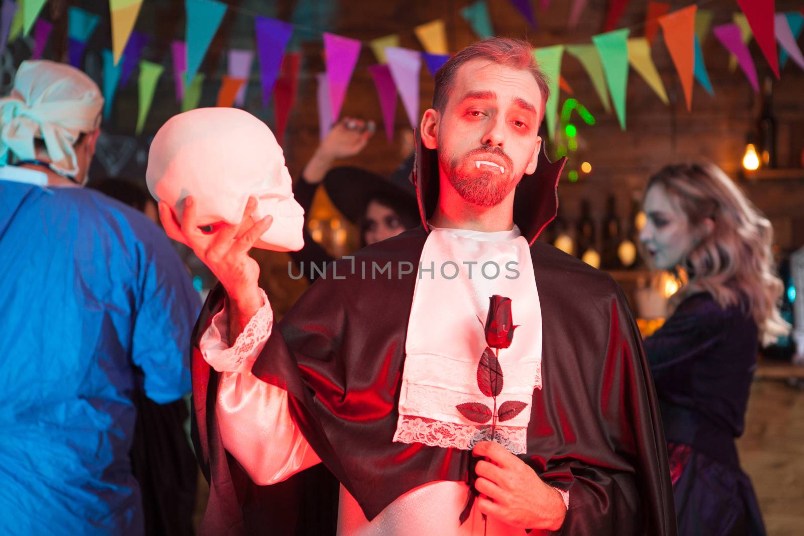 Attractive man dressed up like vampire with a human skull at halloween party. Creepy vampire at halloween celebration.