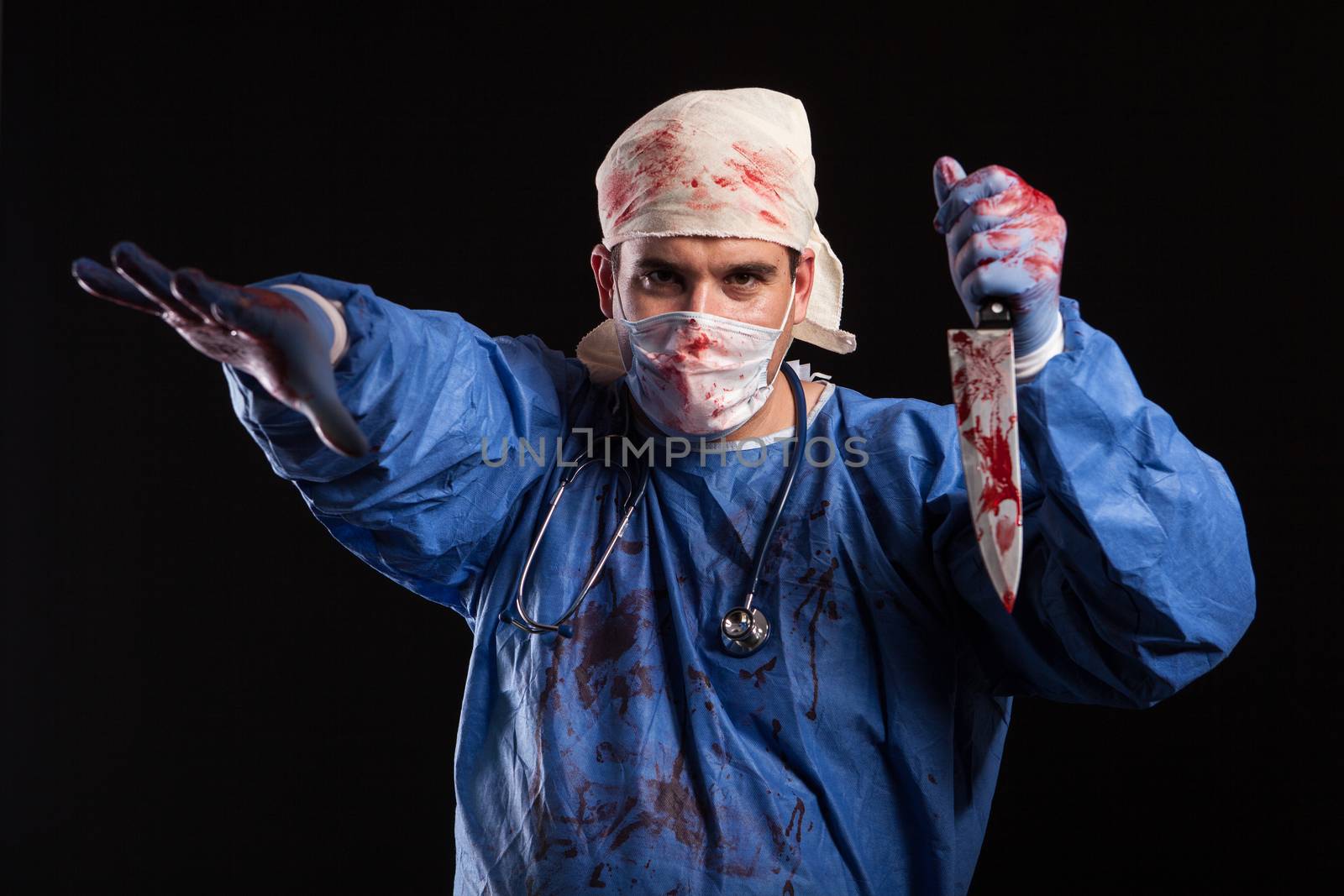 Crazy doctor holding a knife covered in blood in studio over black background. Maniac doctor with mask over his face for halloween.