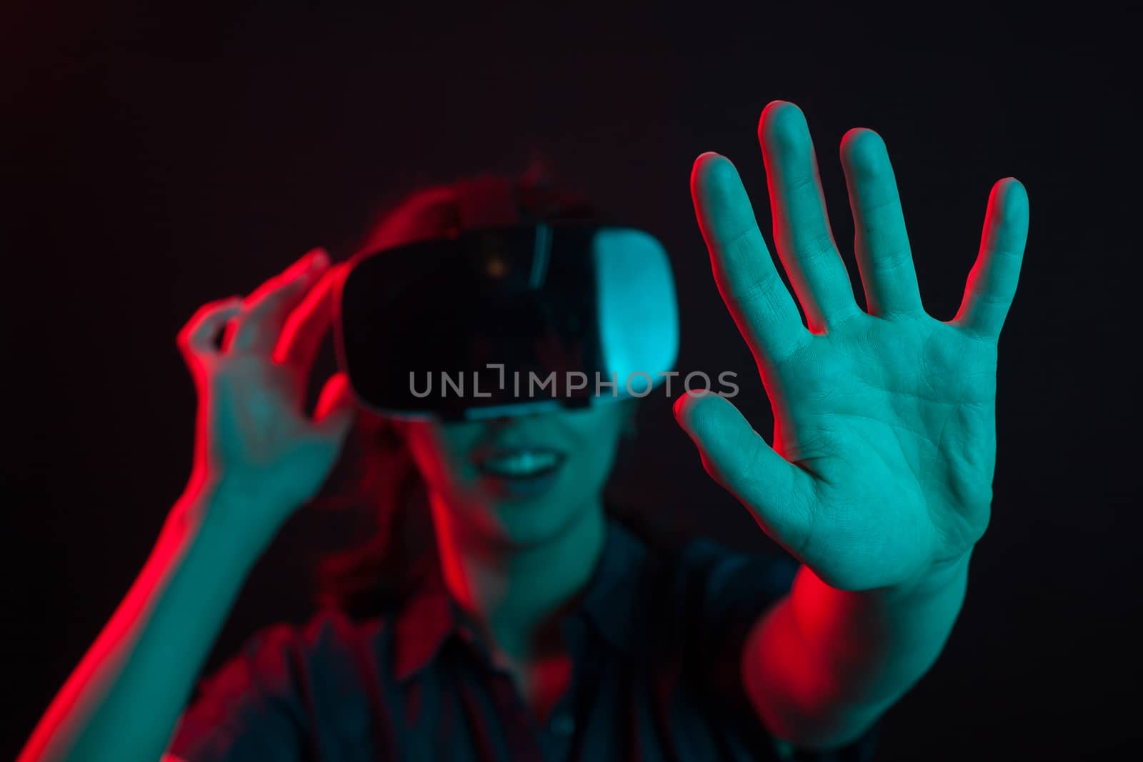 Beautiful young woman enjoying modern lifestyle with virtual reality helmet in studio with creative lighting. Joyfull woman using futuristic gadget. Virtual reality helmet.