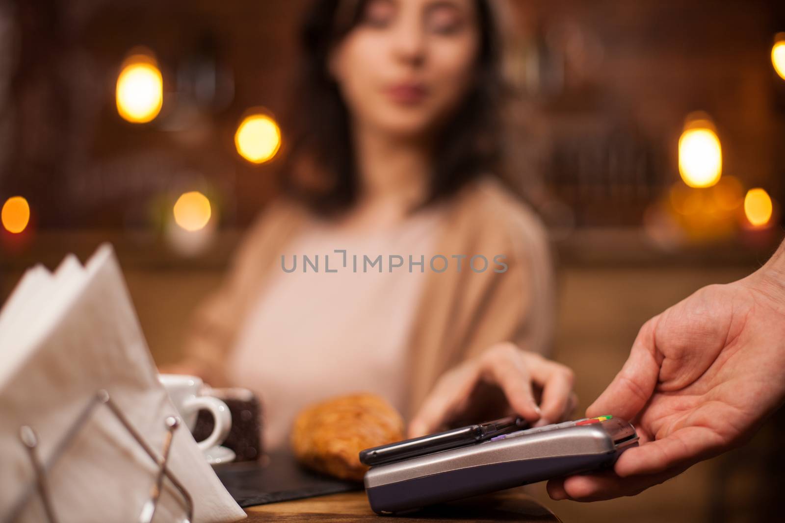Beautiful young woman paying coffee using NFC technology in a coffee shop. Woman paying with mobile phone in a coffee shop.