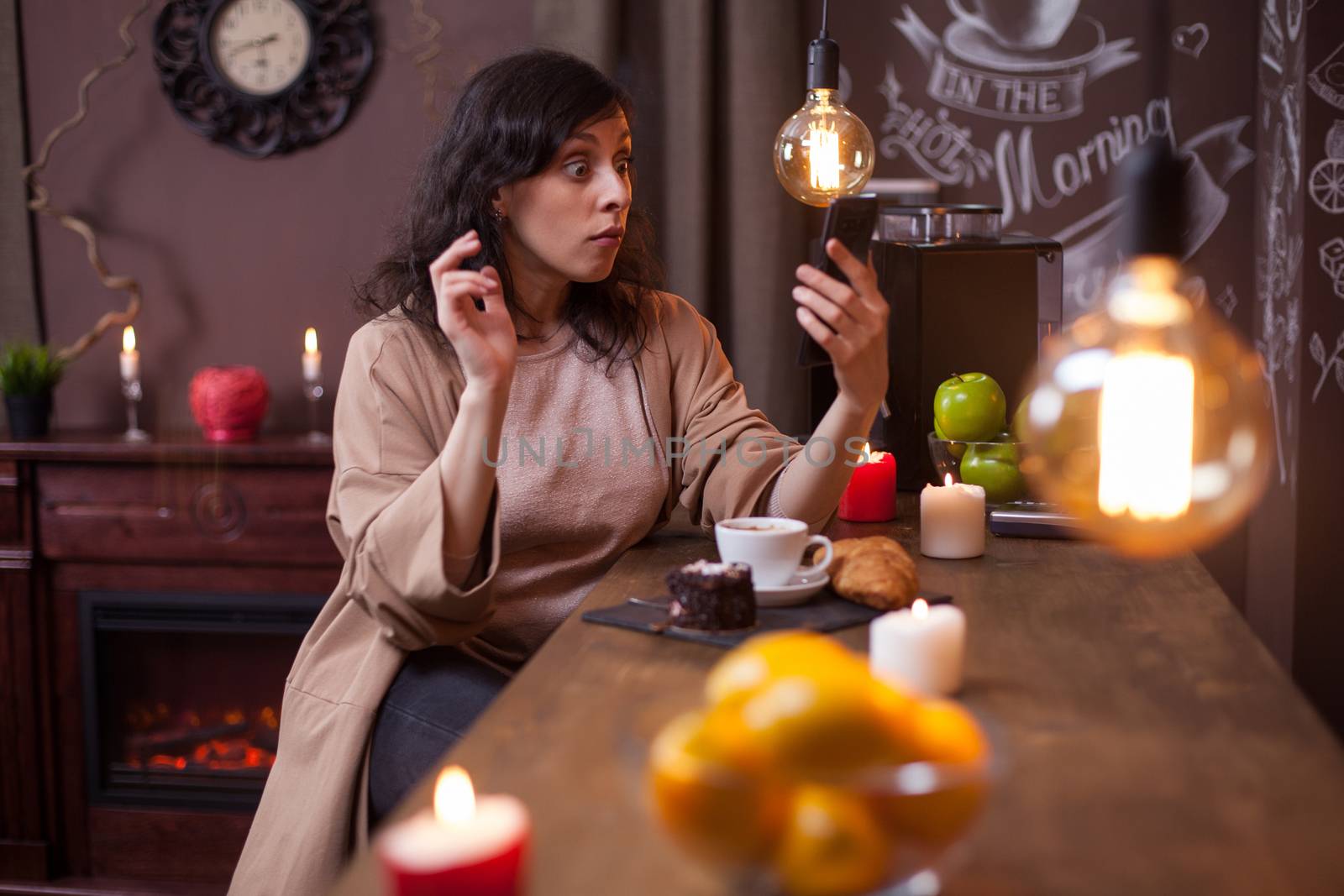 Young pretty woman using mobile phone in a coffee shop and making funny faces. Hipster young woman in a coffee shop.